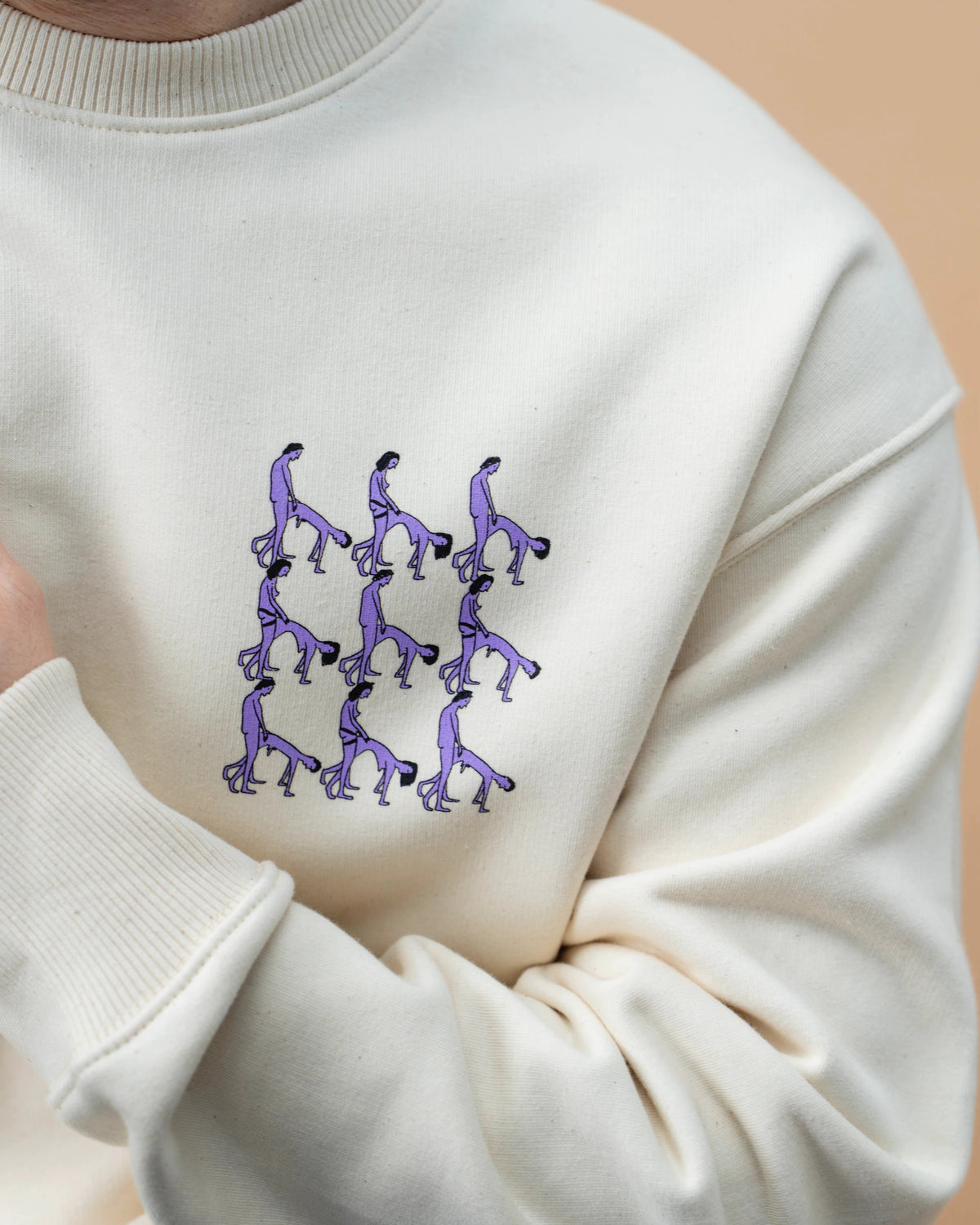 Detailshot of light beige Biweekly crewneck with graphic print of stylized figures in playful poses on the chest, front view