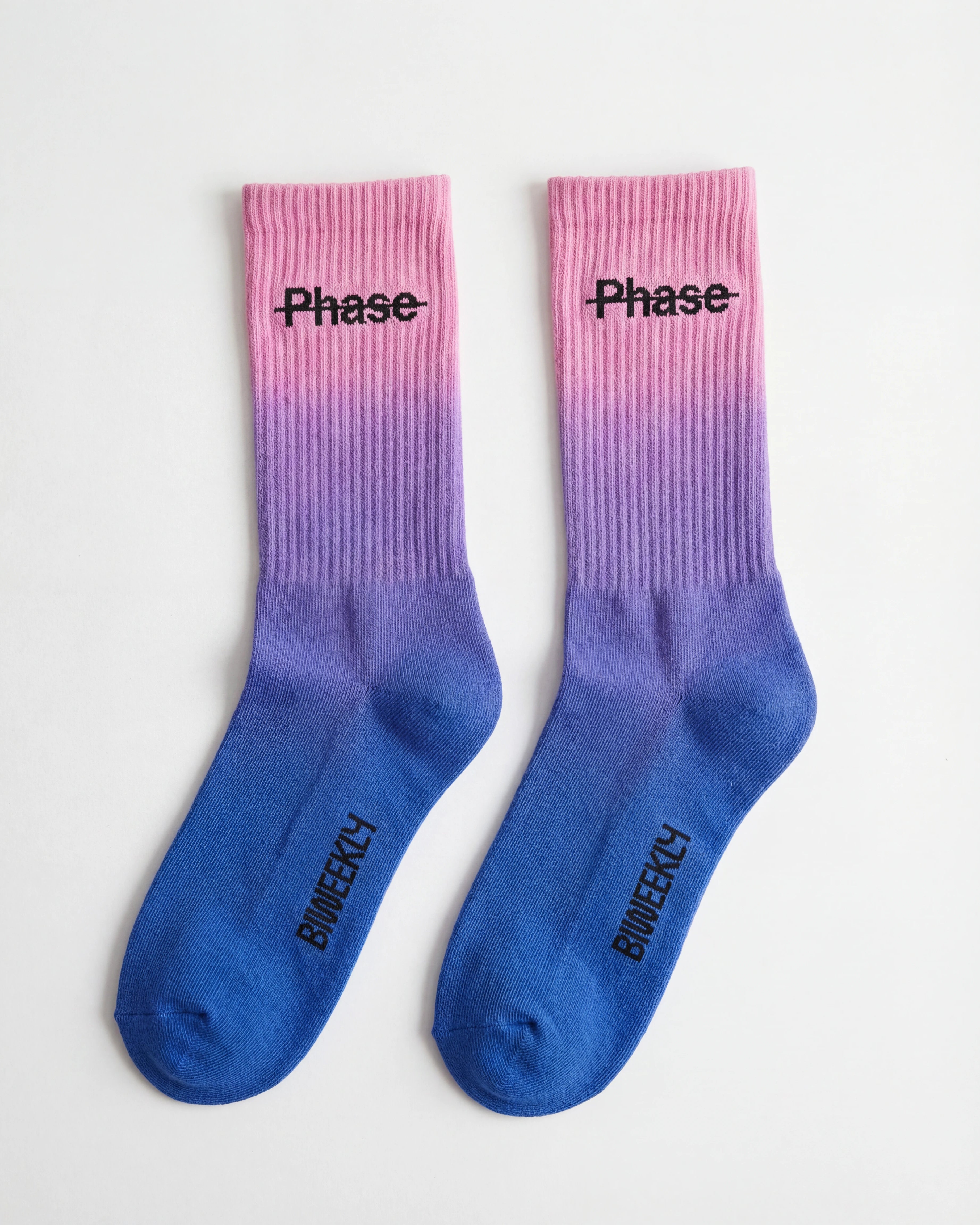 Biweekly socks with watercolor fade from pink to blue with a crossed out "Phase" on the inside and Biweekly logo on the bottom laying flat on a white background
