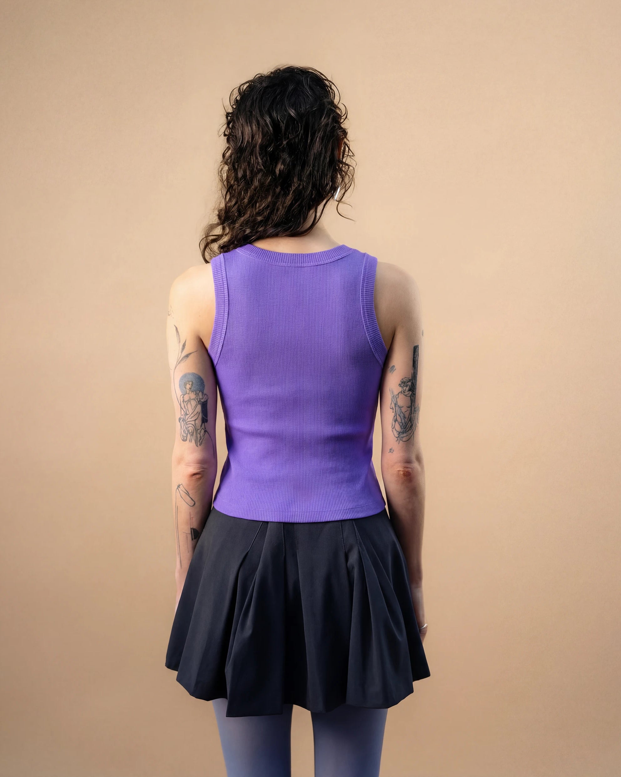 Model wearing a lilac Biweekly tank top, back view against a beige background