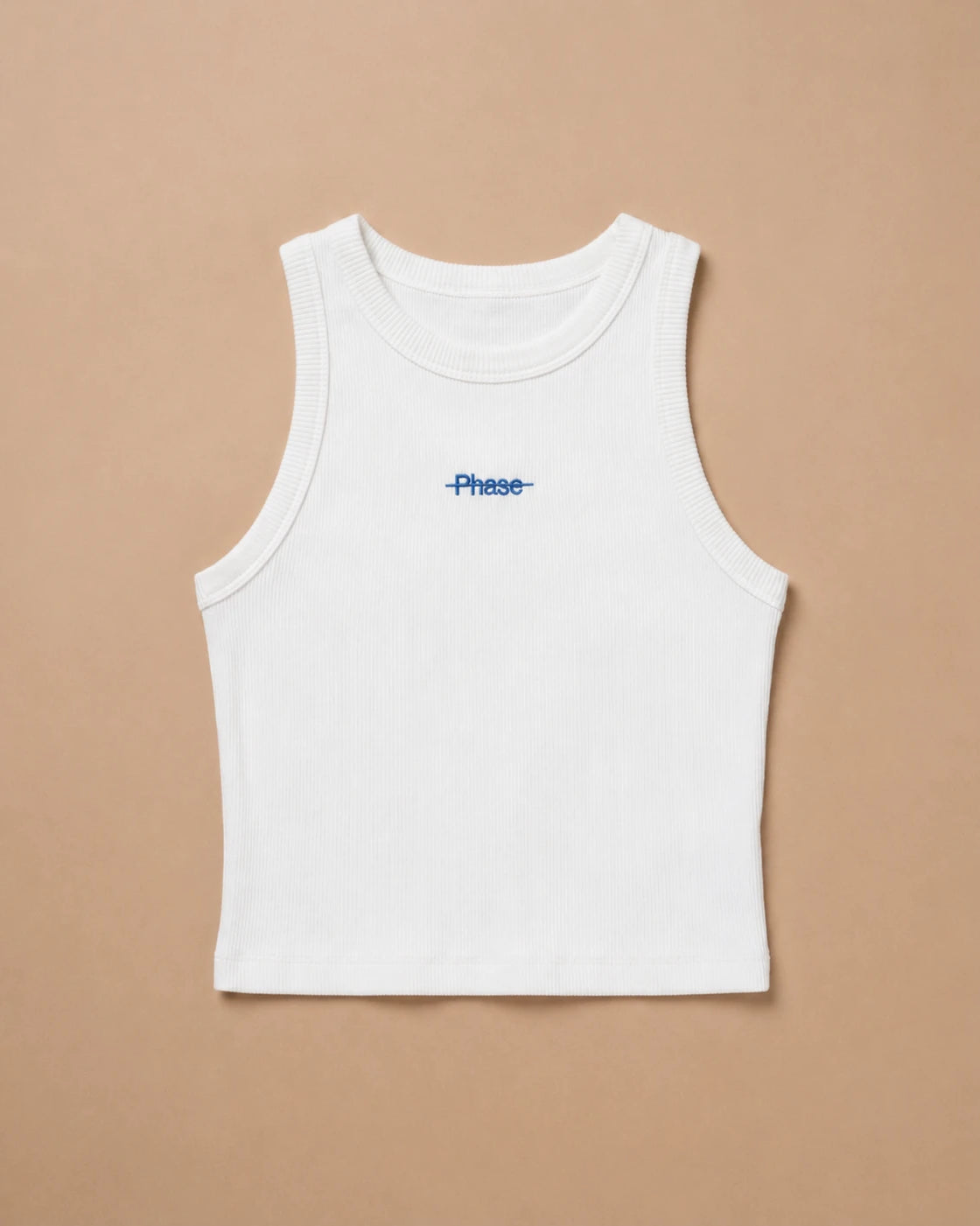 White Biweekly tank top with blue ‘Phase’ text that is crossed out, laying flat against a beige background