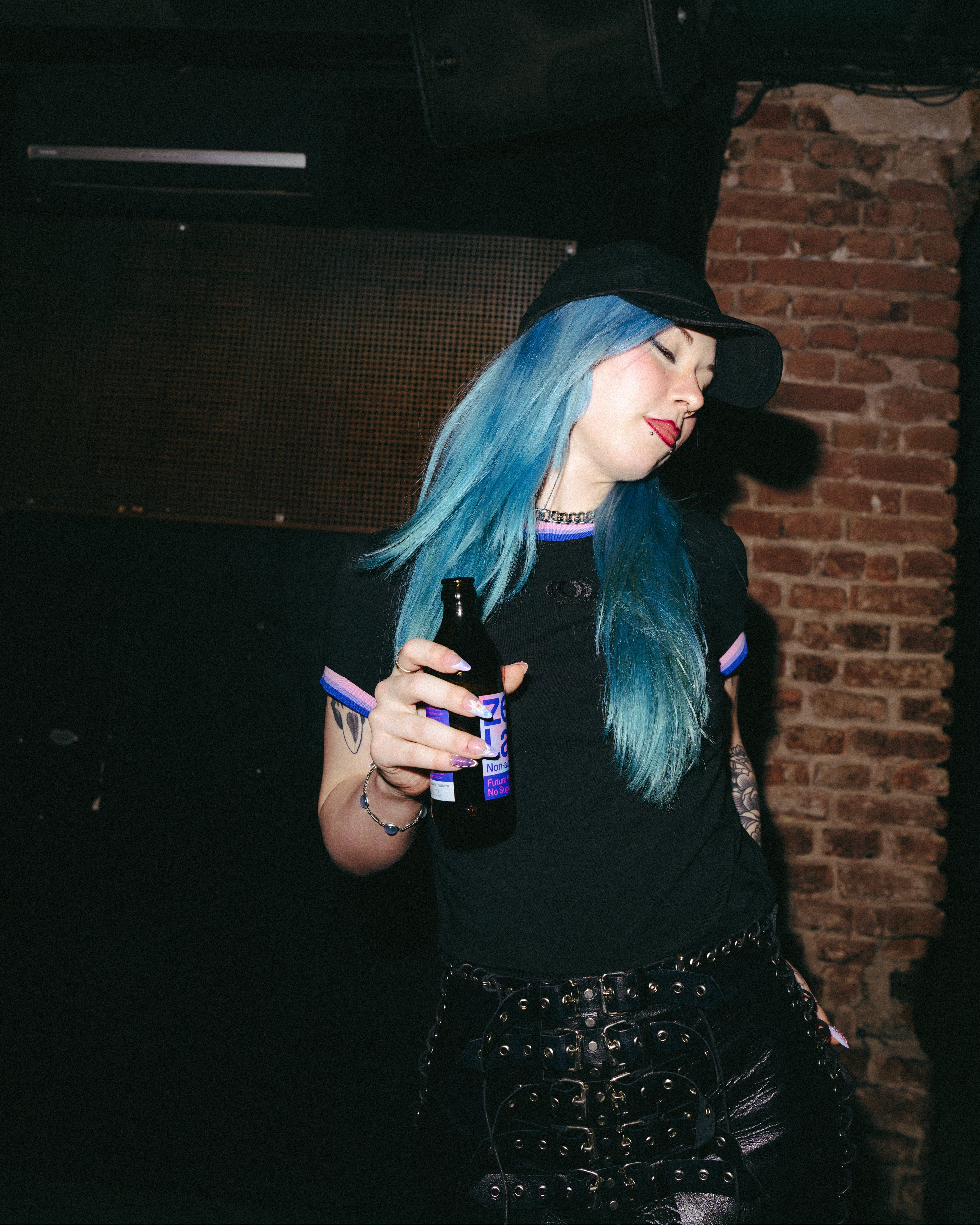 Model wearing a black Biweekly Babytee with bi pride flag trim on the collar and sleeves and black logo in the front, front view in a club scene, dancing