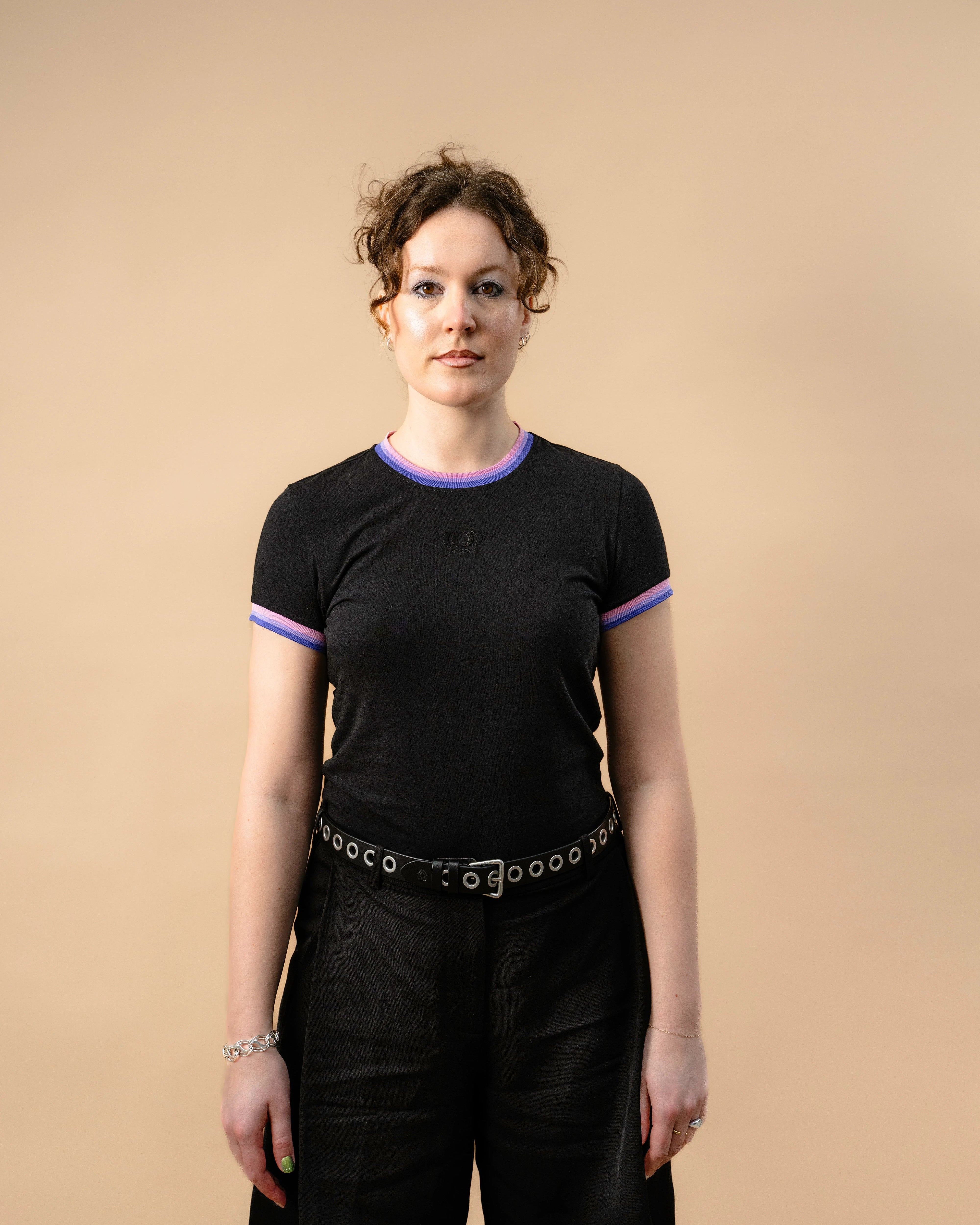 Model wearing a black Biweekly Babytee with bi pride flag trim on the collar and sleeves and black logo in the front, front view against a beige background