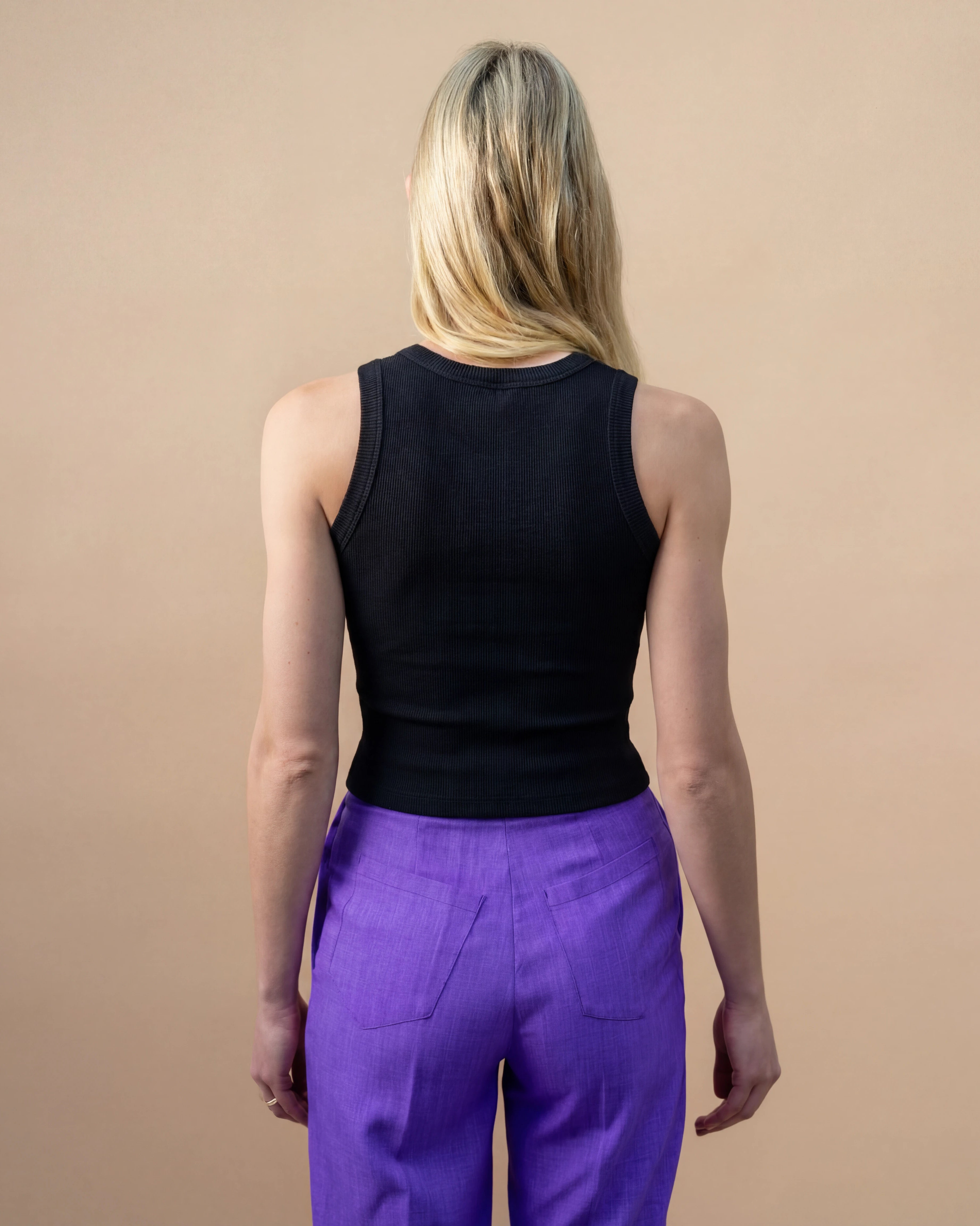 Model wearing a black Biweekly tank top, back view against a beige background