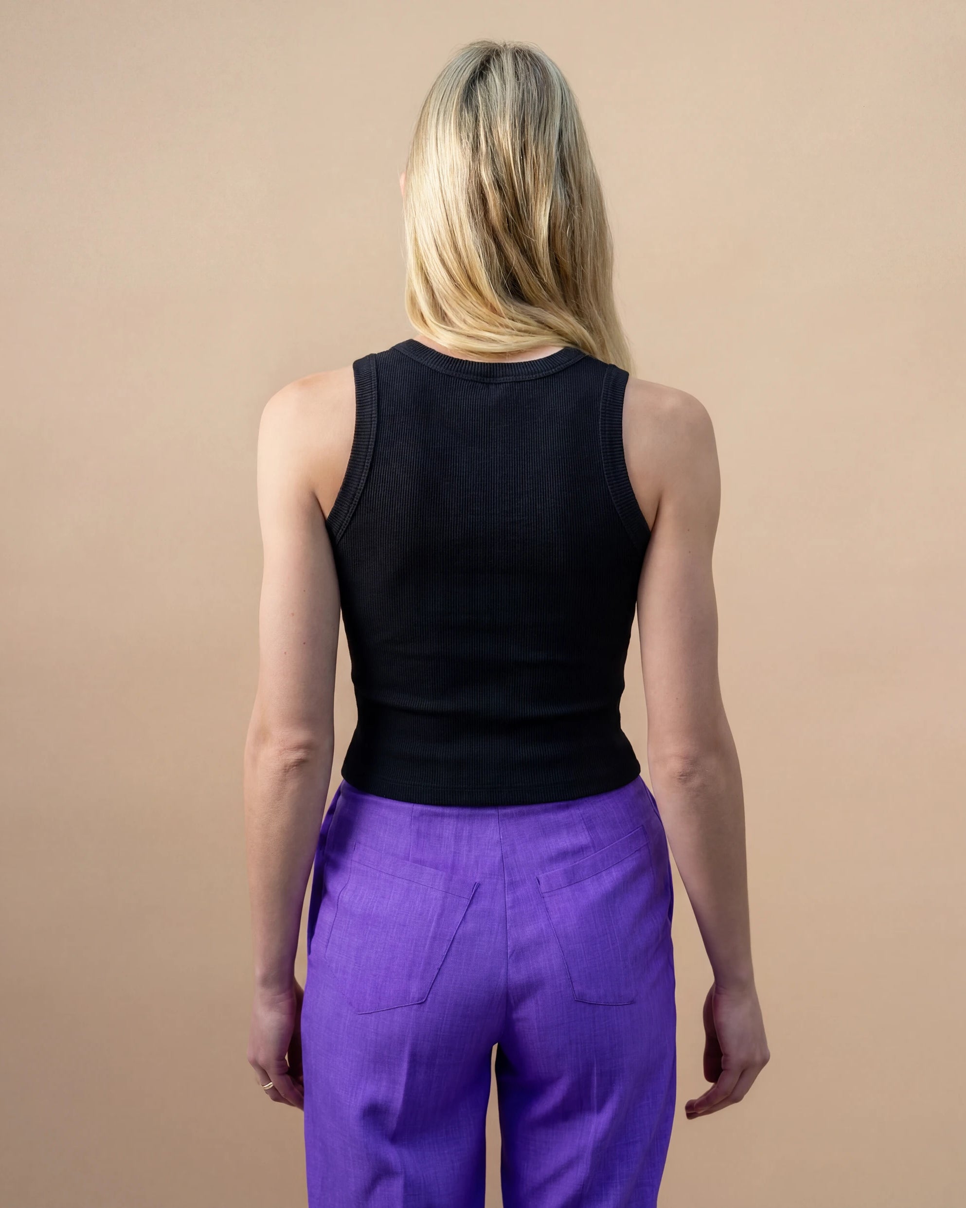 Model wearing a black Biweekly tank top, back view against a beige background