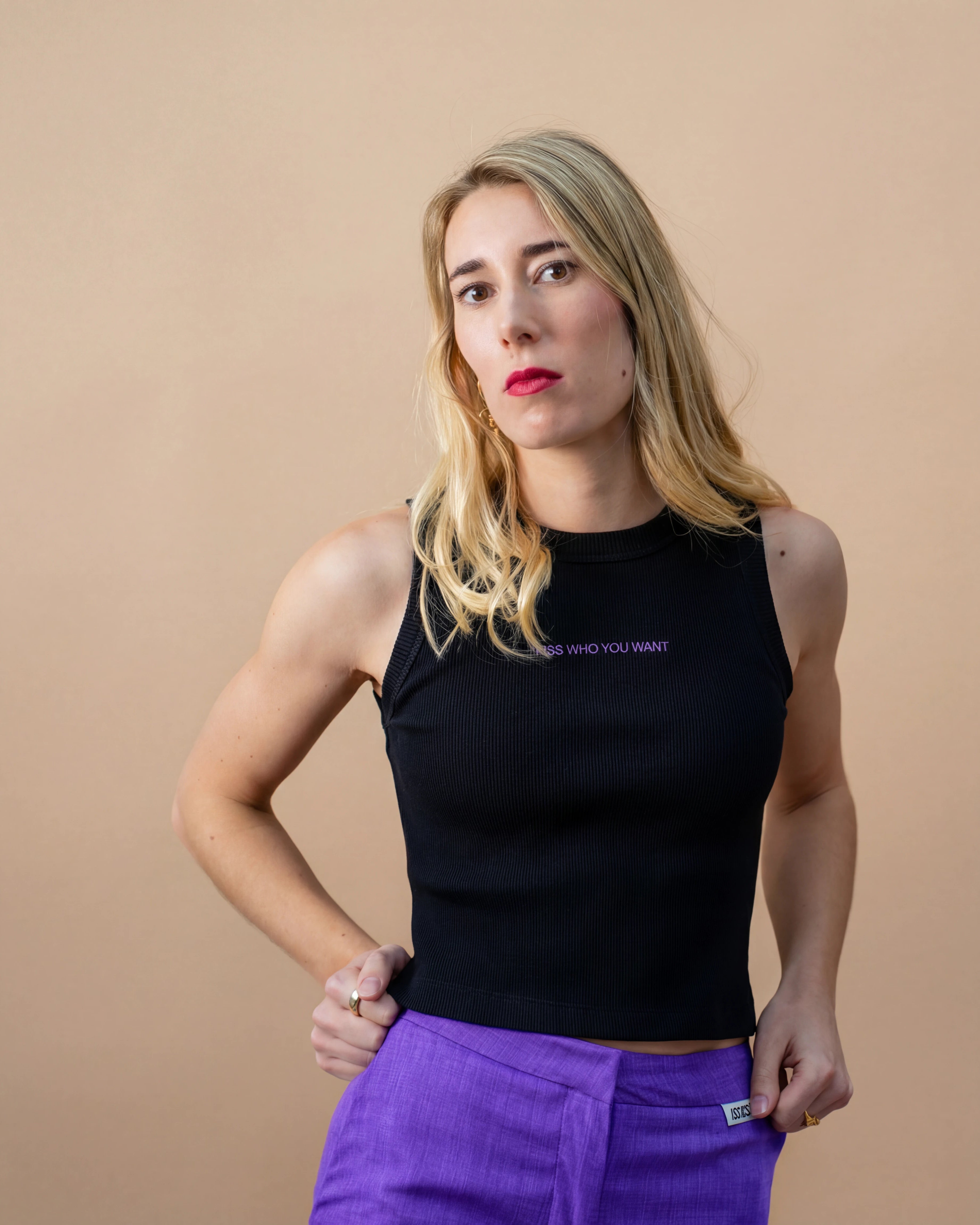 Model wearing a black Biweekly tank top with lilac ‘Kiss Who You Want’ text, front view against a beige background