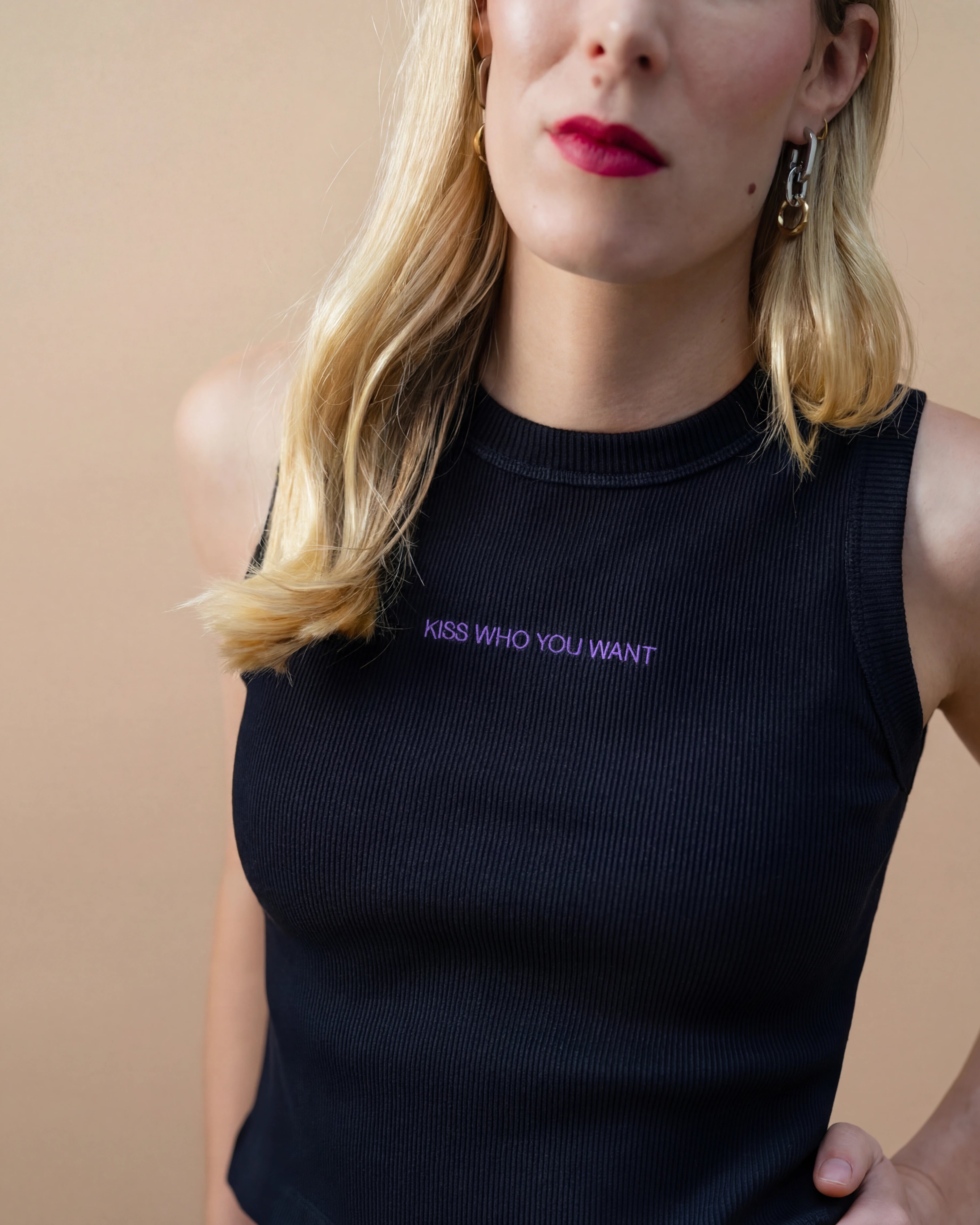 Detail view of a black Biweekly tank top with lilac ‘Kiss Who You Want’ text against beige background