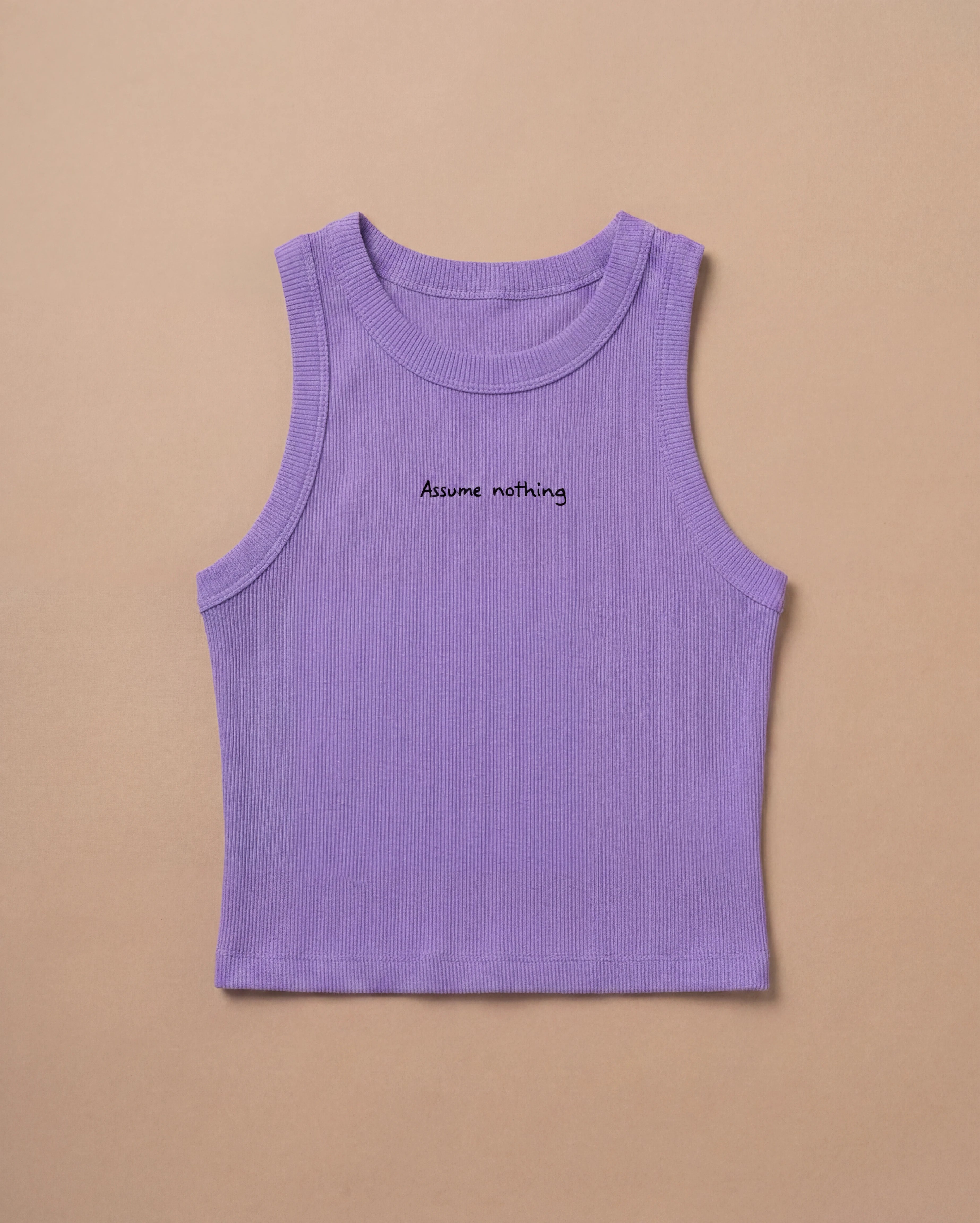 Lilac Biweekly tank top with black ‘Assume nothing’ text laying flat on beige background
