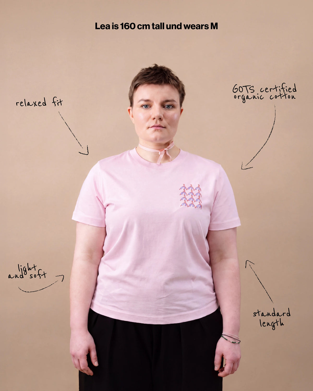 Model wearing light pink Biweekly T-shirt with clit graphic print on right chest area, front view, against beige background with text that gives information about the short
