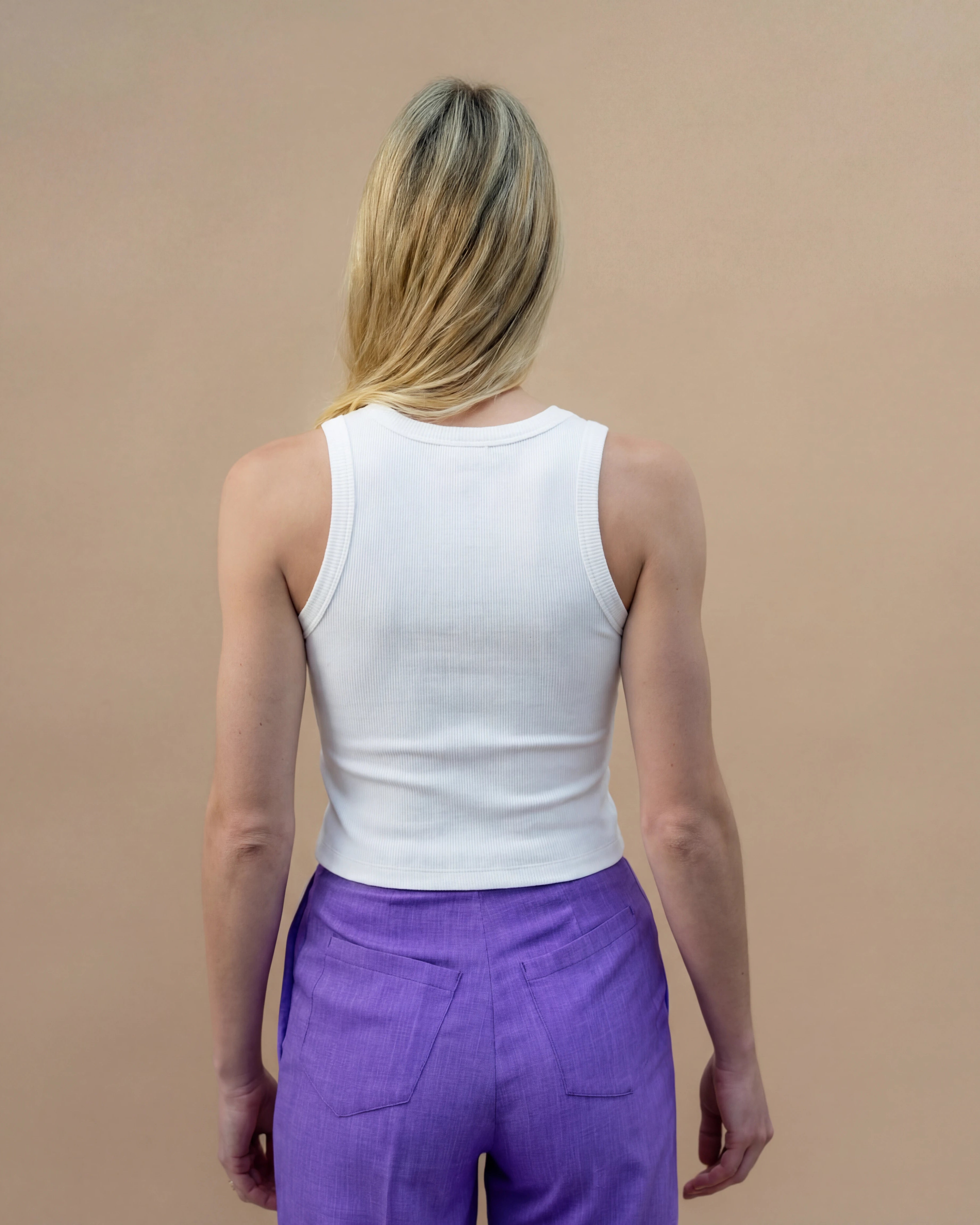 Model wearing a white Biweekly tank top, back view against a beige background