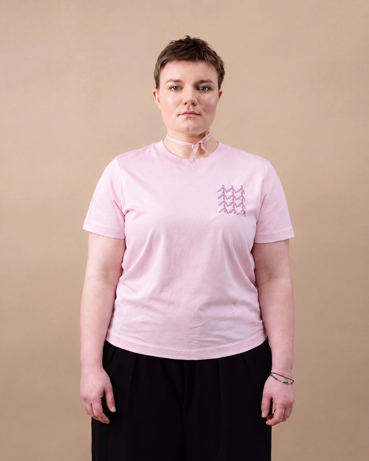 Model wearing light pink Biweekly T-shirt with clit graphic print on right chest area, front view, against beige background