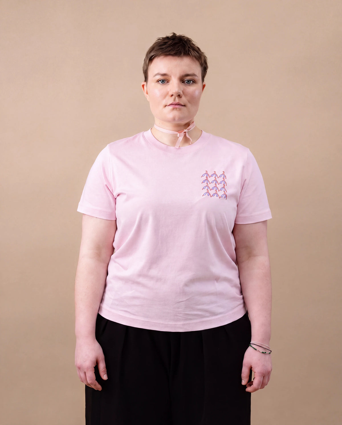 Model wearing light pink Biweekly T-shirt with clit graphic print on right chest area, front view, against beige background