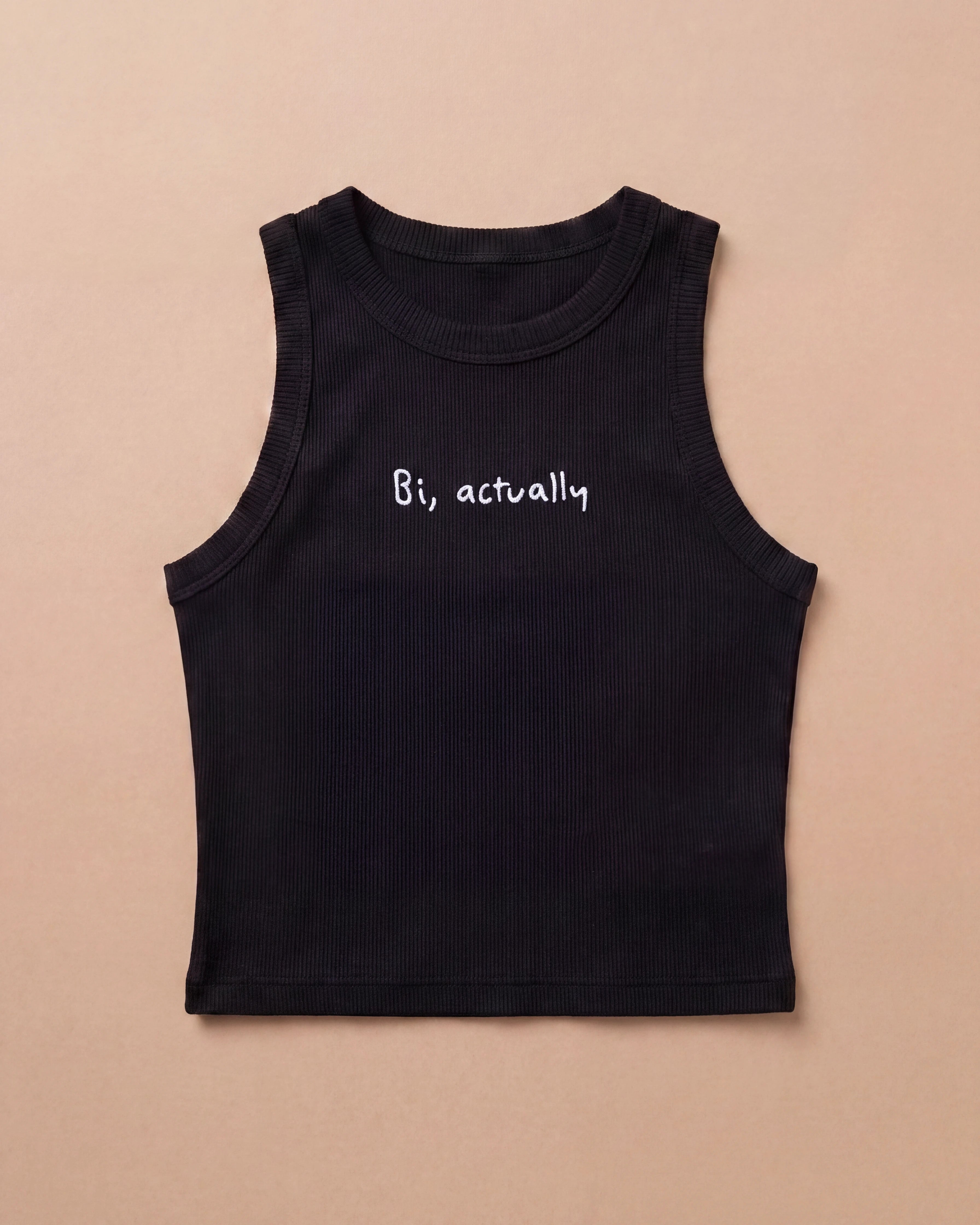 Black Biweekly tank top with white ‘Bi, actually’ text, laying flat against a beige background