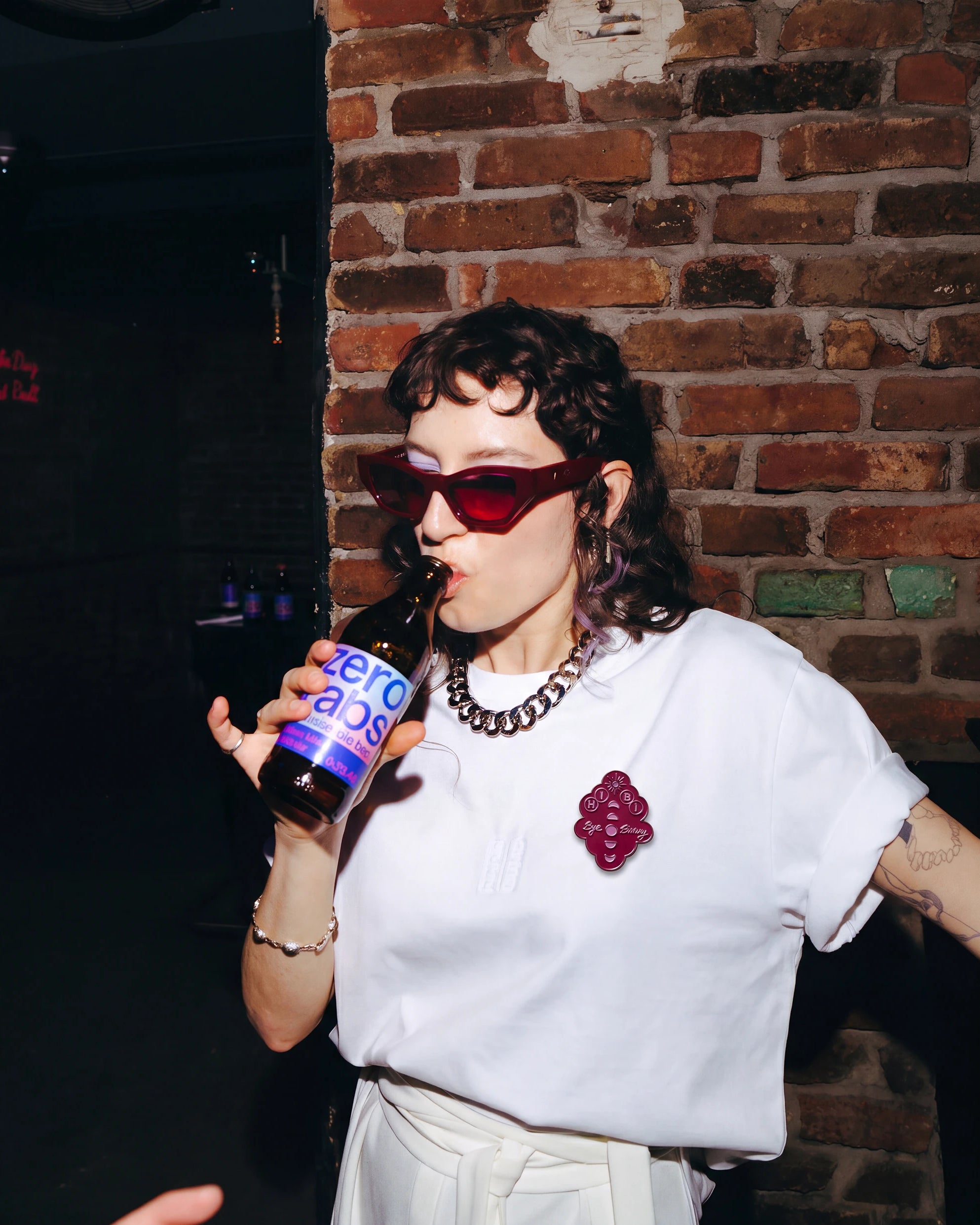 Model wearing burgundy Biweekly pin with 'Hi Bi - Bye Binary' text and moon phase illustration on a white Biweekly Shirt.