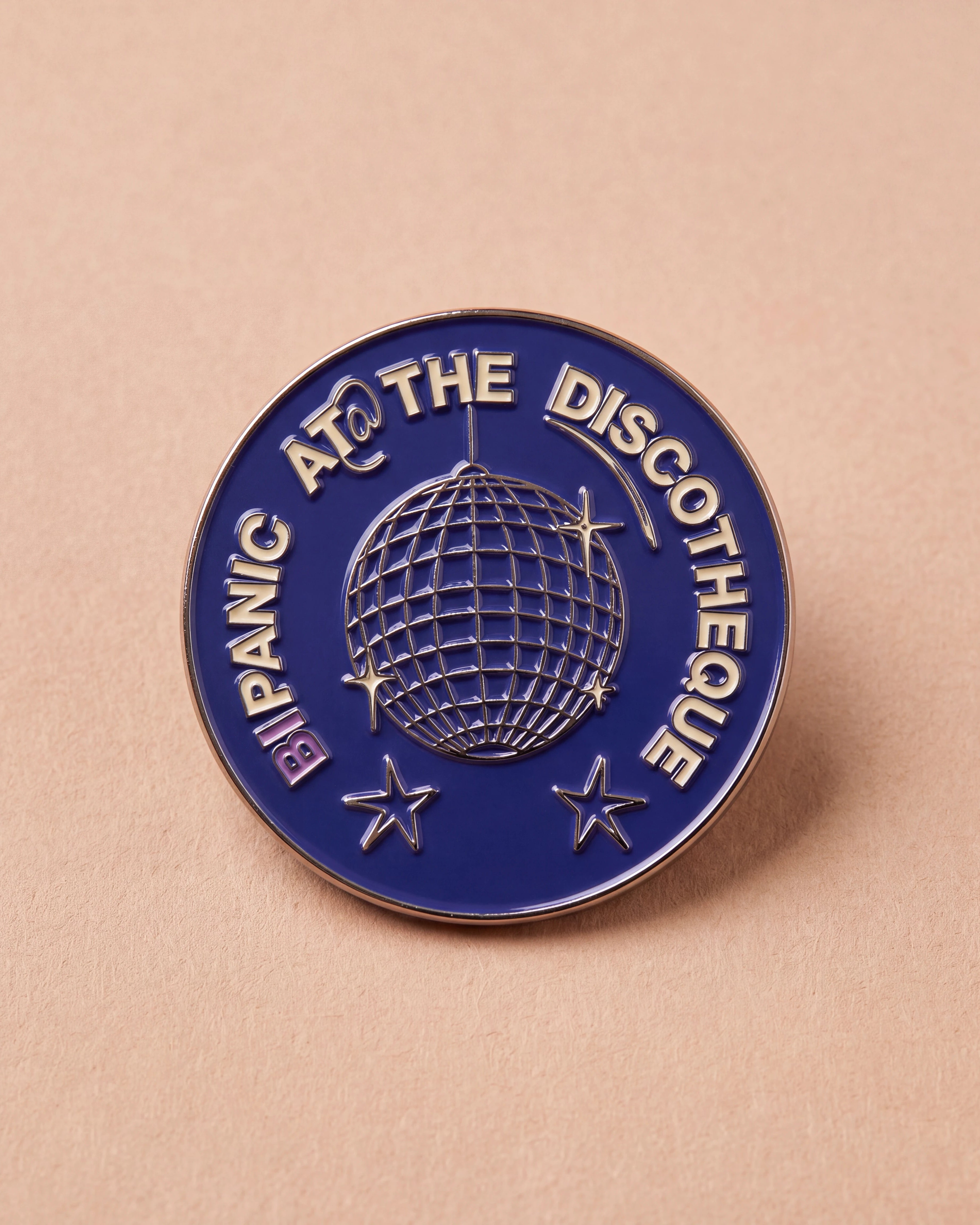 Blue Biweekly pin with 'Bipanic at the discotheque' text and disco ball illustration, flatlay against a beige background