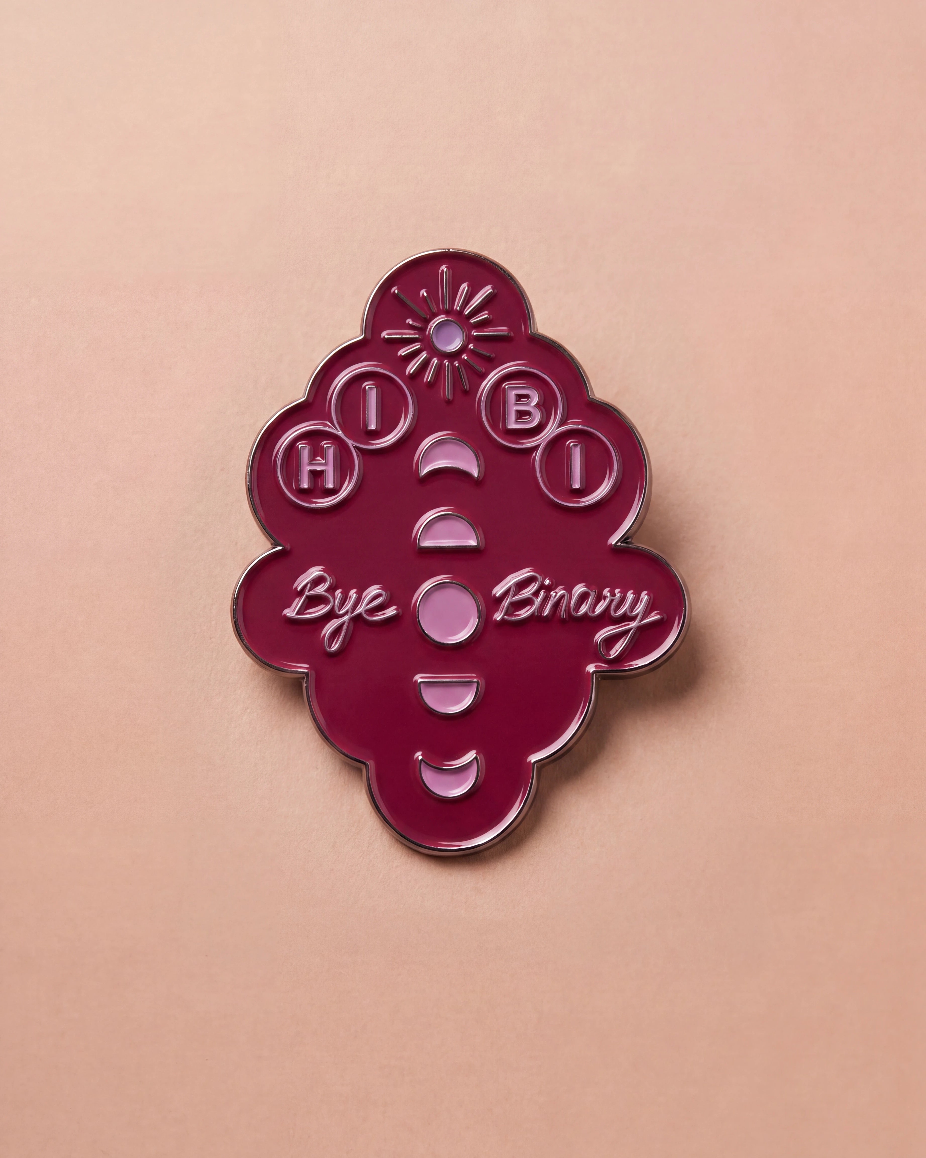 Burgundy Biweekly pin with 'Hi Bi - Bye Binary' text and moon phase illustration, flatlay against a beige background