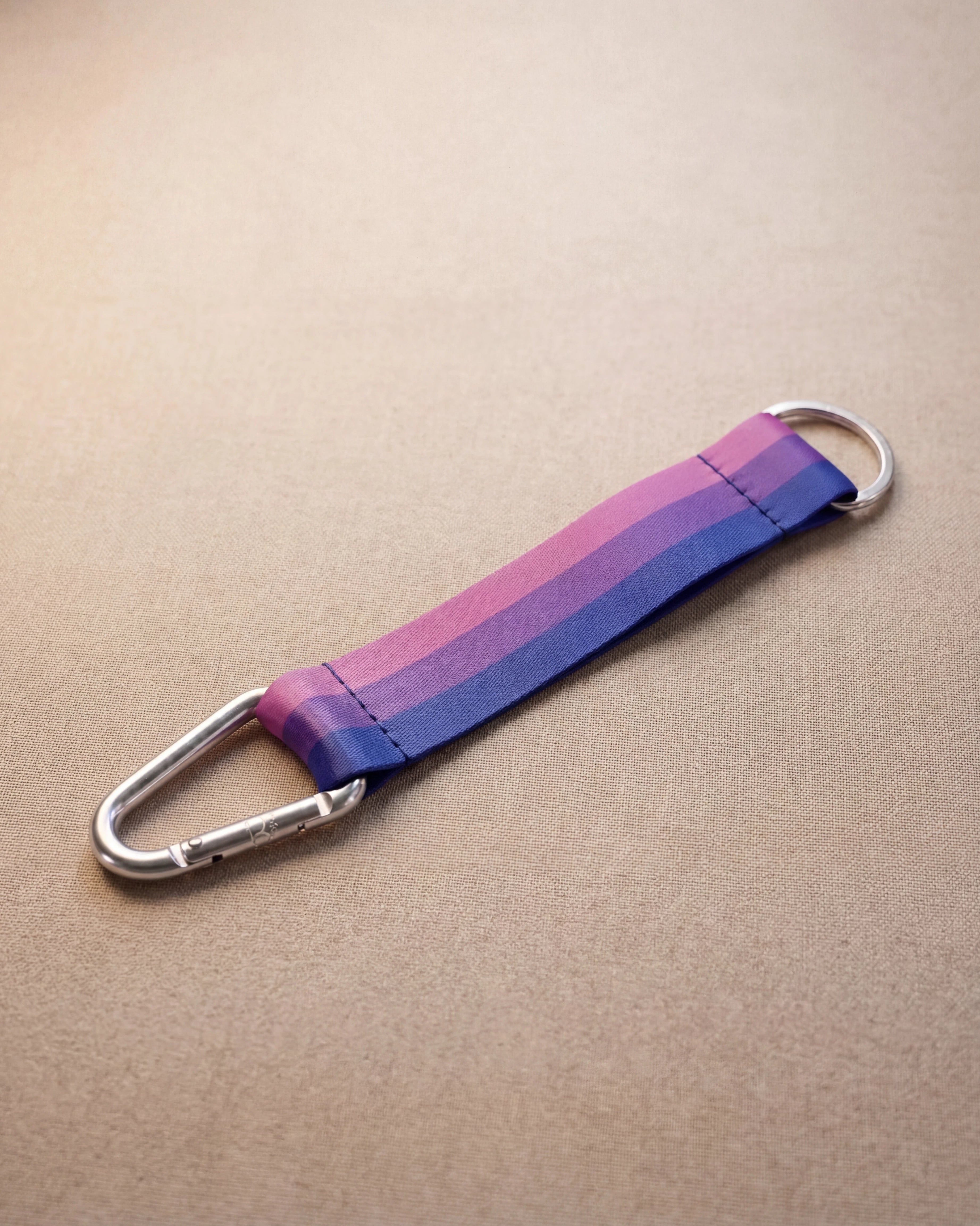 Keychain in bi pride flag colors with silver carabiner and blue yarn laying on beige surface