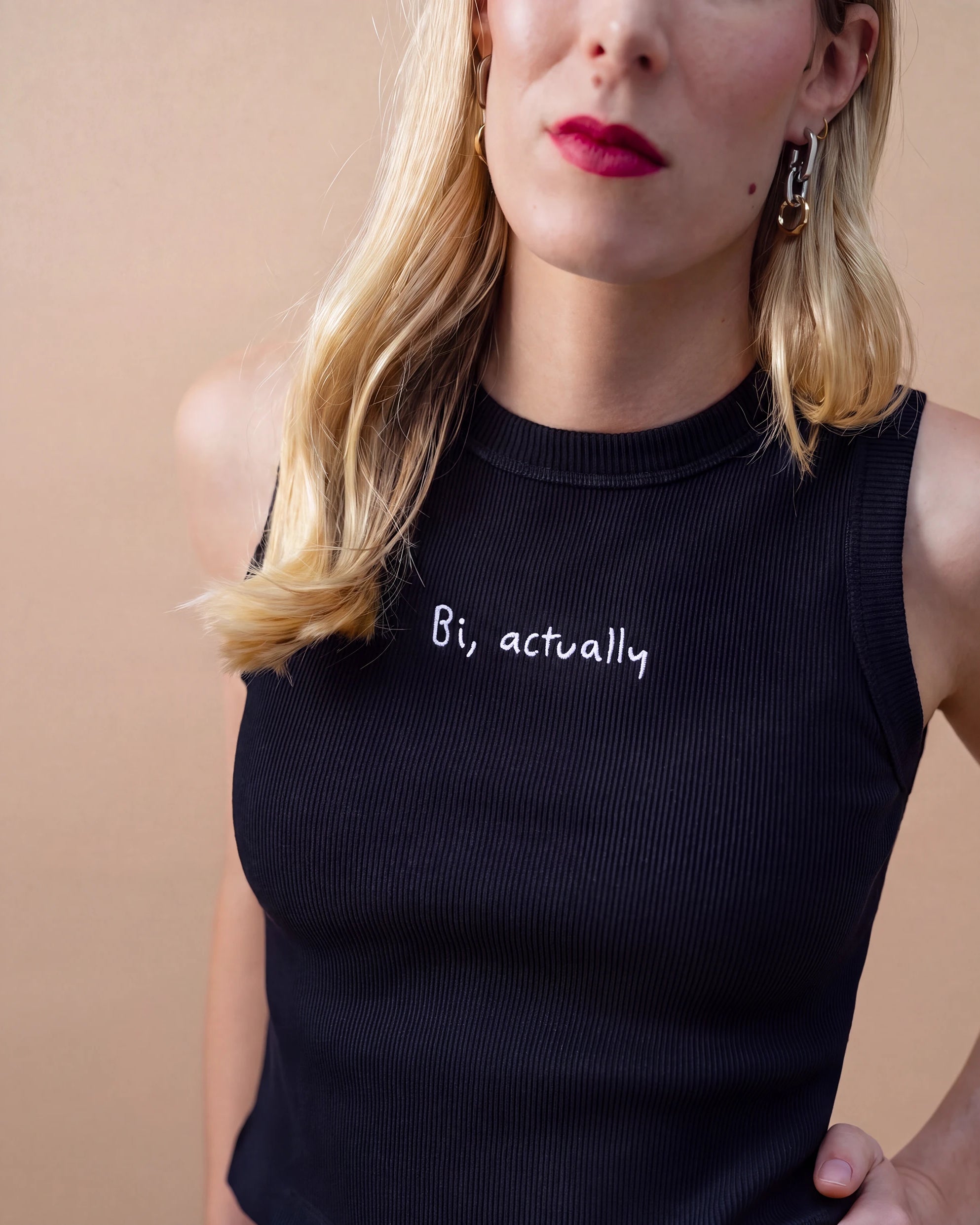Detail view of a black Biweekly tank top with white ‘Bi, actually’ text against beige background