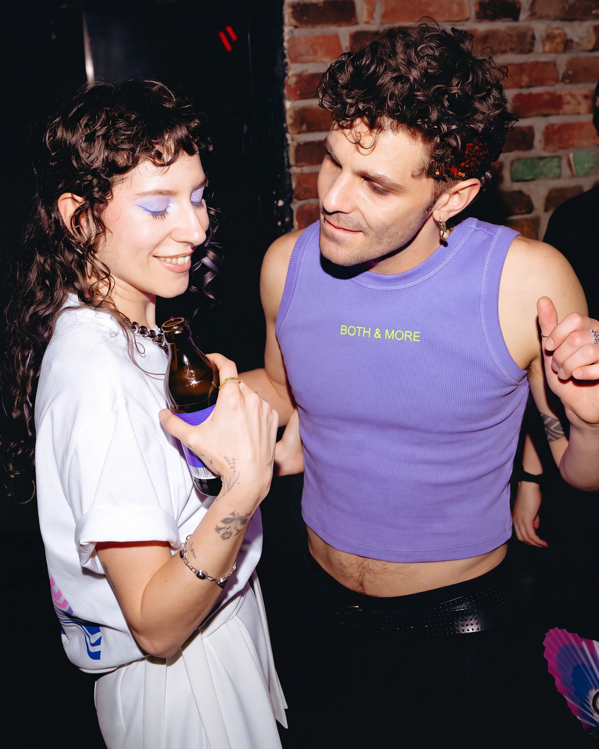 Model wearing a lilac Biweekly tank top with yellow ‘BOTH & MORE’ text, front view dancing with another model in a cub scene