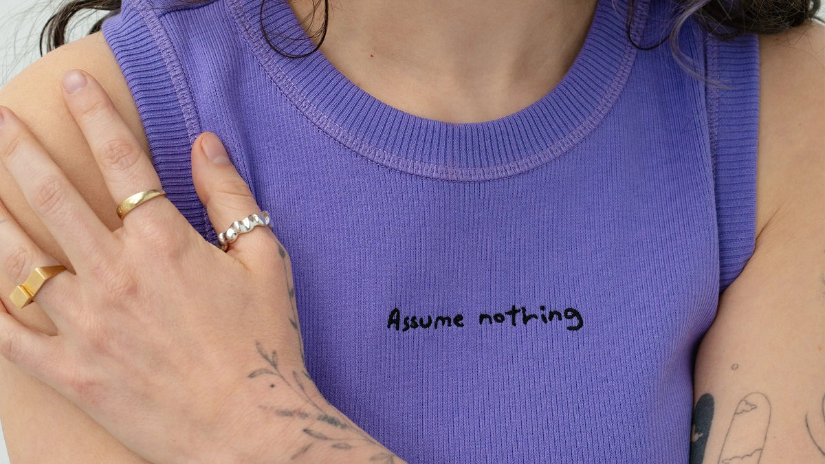 girl wearing Biweekly "assume nothing" top, close up of embroidery and hands placed on shoulder