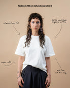 Model wears an oversized white Biweekly T-shirt with white ‘BiBi’ logo, front view against a beige background. With text that gives information on the shirt. 