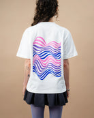 Model wears an oversized white Biweekly T-shirt with wavy bi pride flag graphic print and `Perfectly Not Straight` text on the print, back view against a beige background