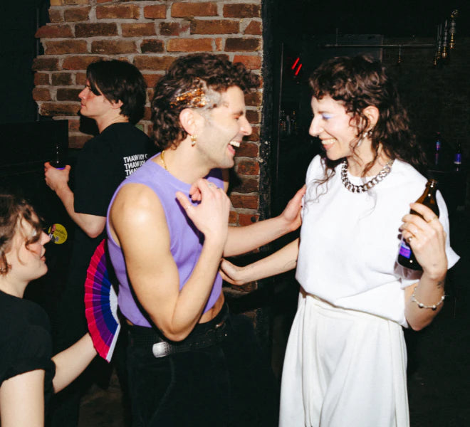 Two models laughing and touching each others arms waring a lilac Biweekly croptop and a white oversized Shirt in a cöub scenario with two other people in the background