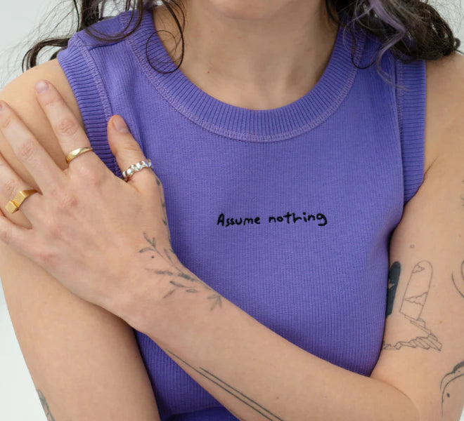 Detailshot of model wearing a lilac Biweekly tank top with black ‘Assume nothing’ text, front view against a white background