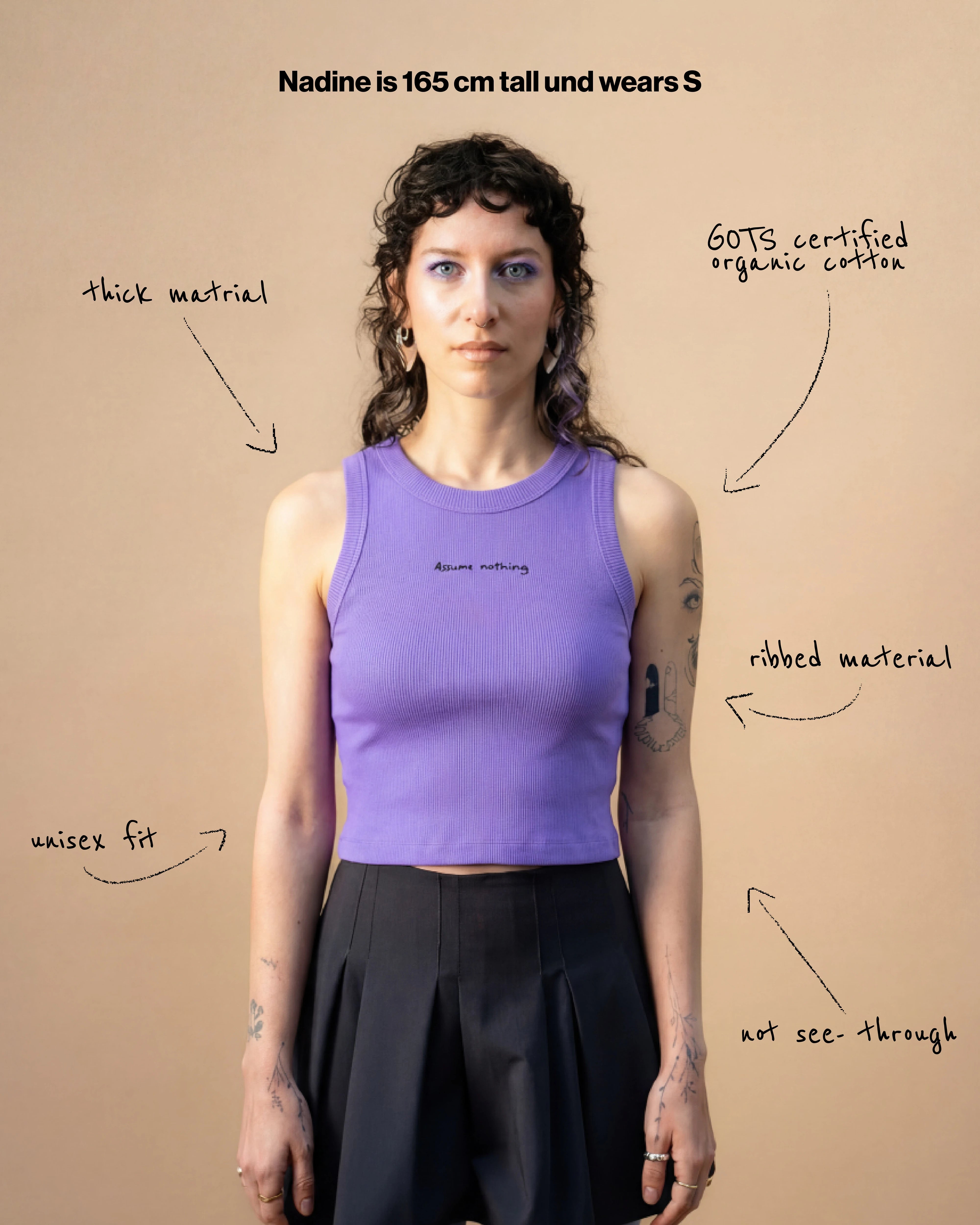 Model wearing a lilac Biweekly tank top with black ‘Assume nothing’ text, front view against a beige background. Text that gives information about the top. 