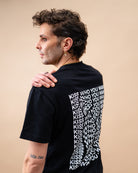 Model wearing a black oversized Biweekly T-shirt with distorted repeated ‘Kiss Who You Want’ text print, side view against a beige background