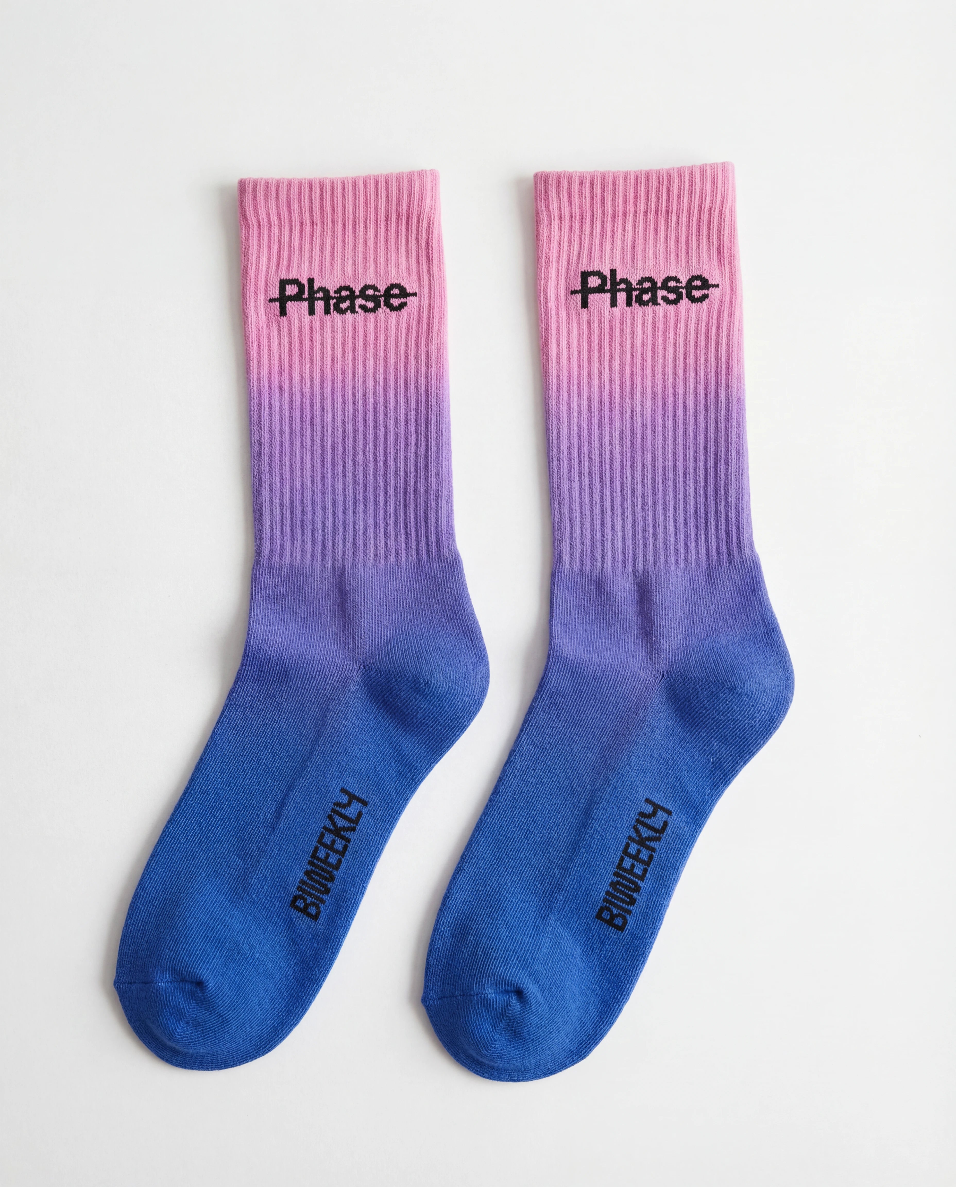 Biweekly socks with watercolor fade from pink to blue with a crossed out "Phase" on the inside and Biweekly logo on the bottom laying flat on a white background