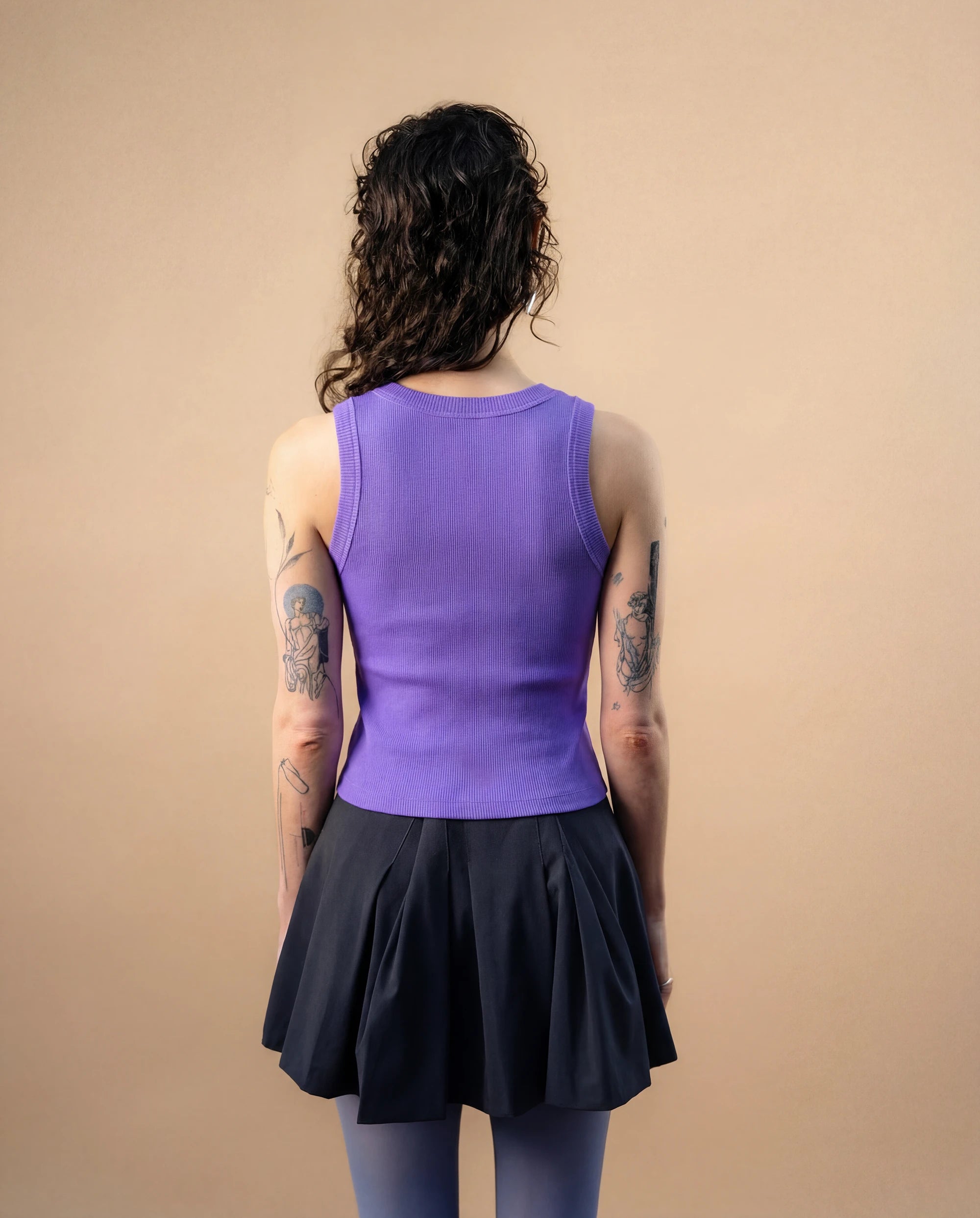Model wearing a lilac Biweekly tank top, back view against a beige background