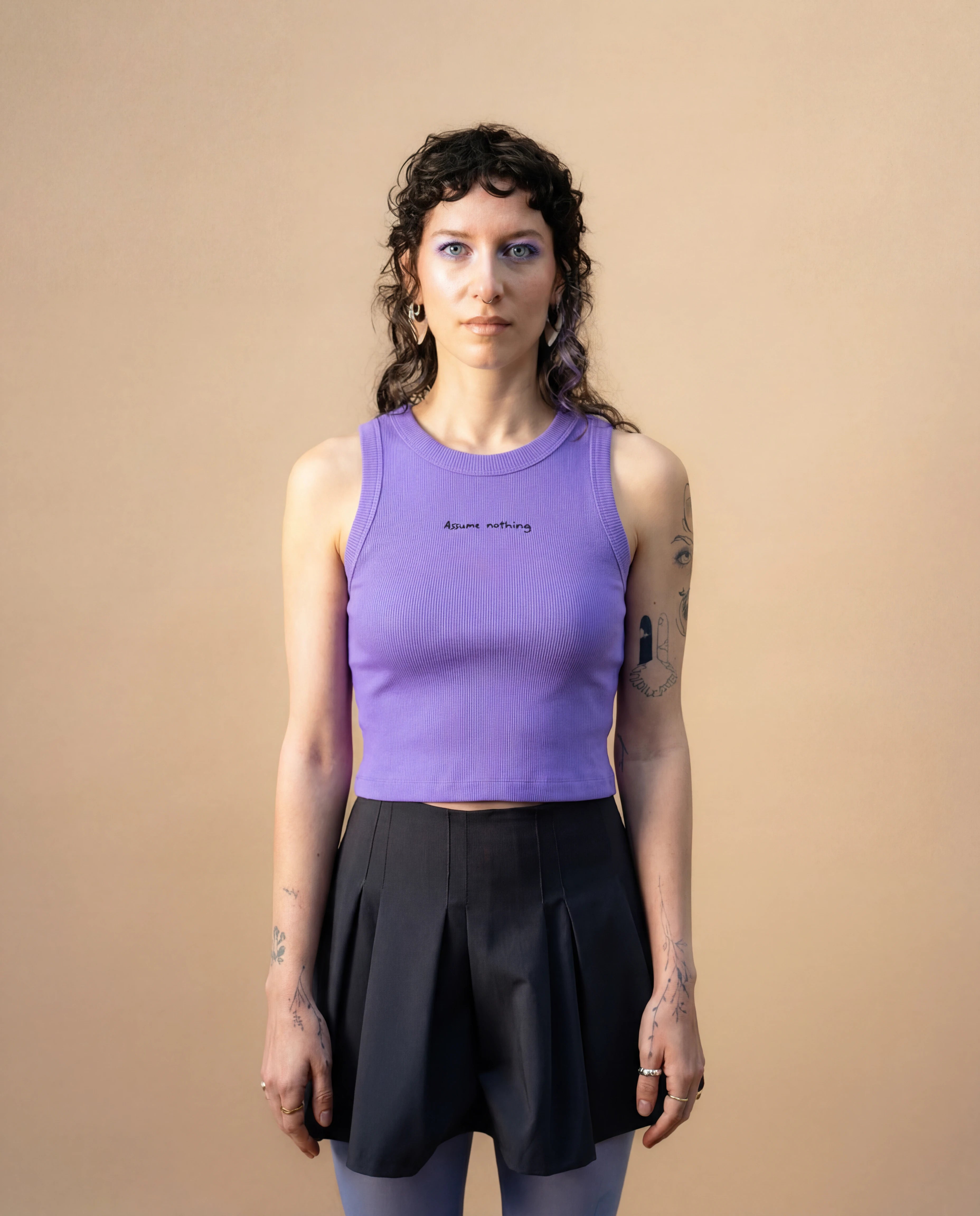Model wearing a lilac Biweekly tank top with black ‘Assume nothing’ text, front view against a beige background