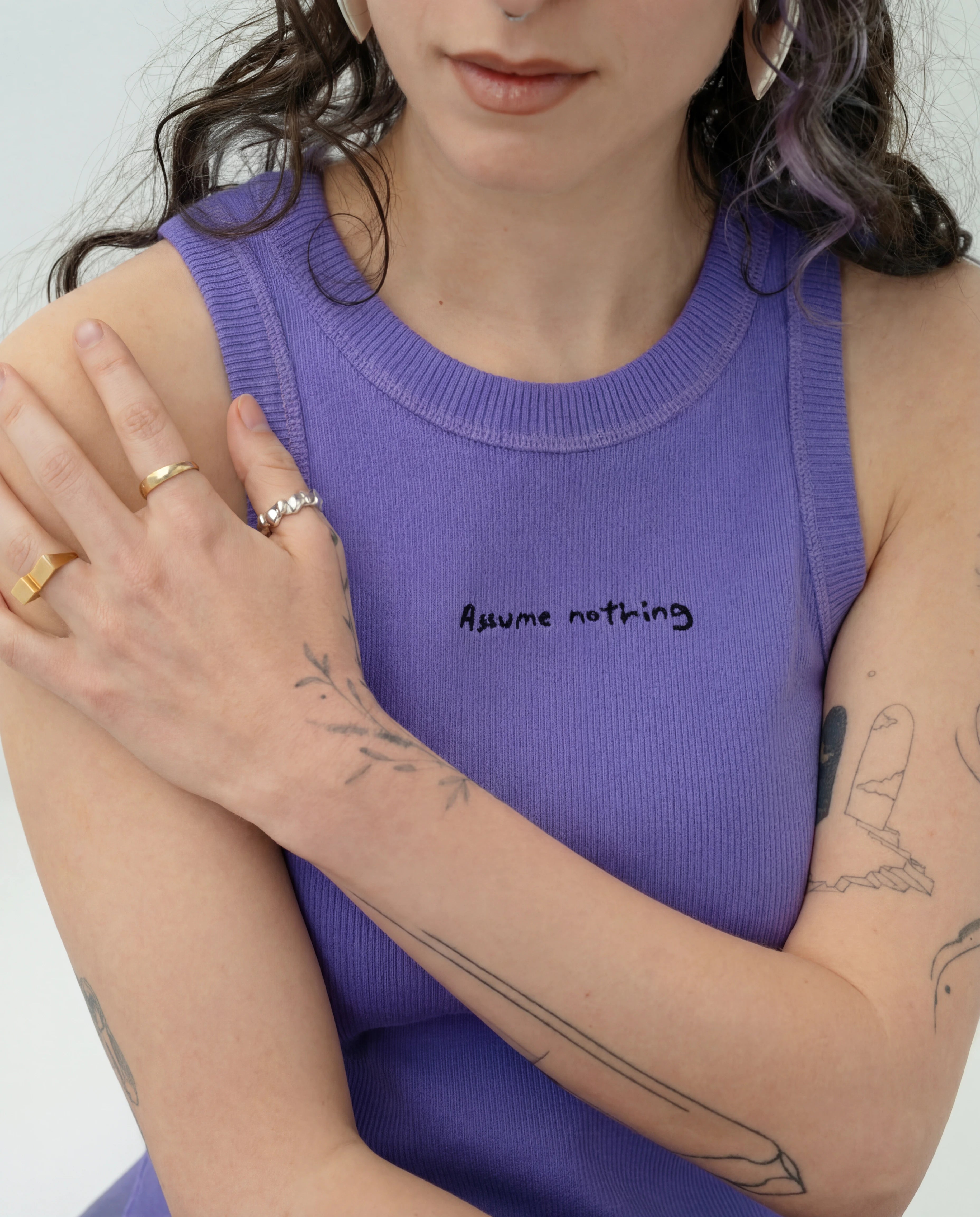 Detailshot of model wearing a lilac Biweekly tank top with black ‘Assume nothing’ text, front view against a white background