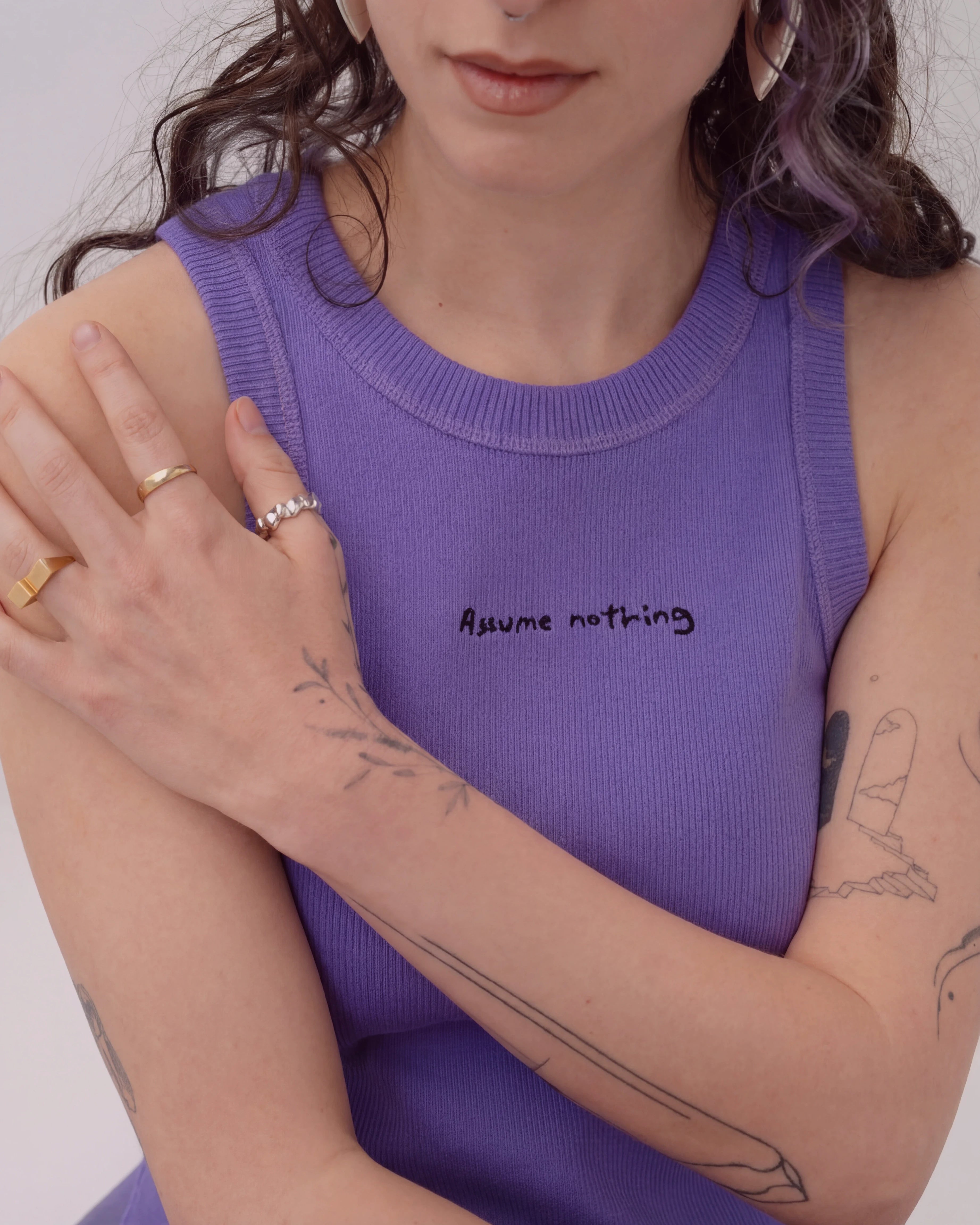 Detailshot of model wearing a lilac Biweekly tank top with black ‘Assume nothing’ text, front view against a white background