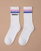 Flatlay picture of white Biweekly socks with bi pride flag stripes and text logo underneath, against a beige background