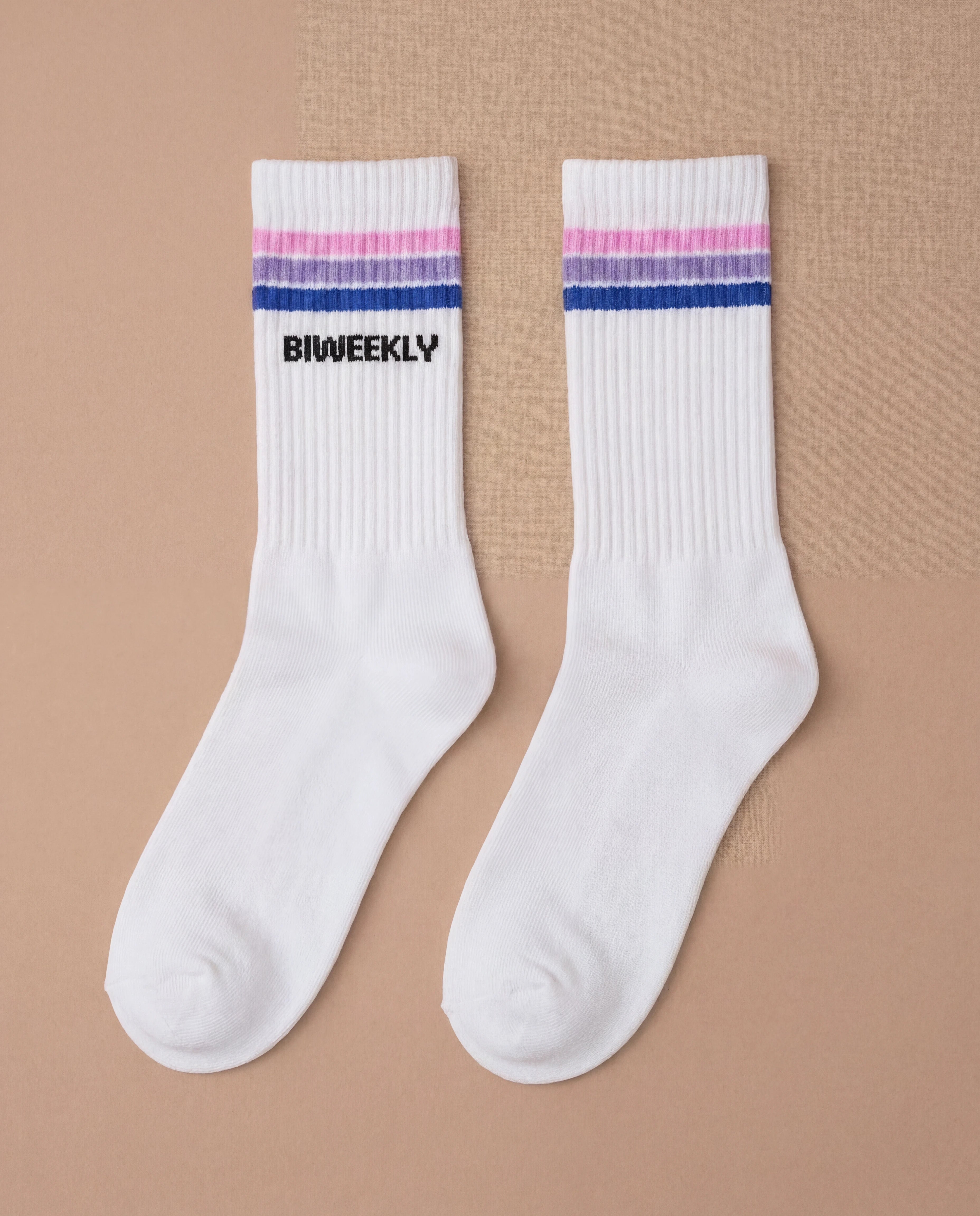 Flatlay picture of white Biweekly socks with bi pride flag stripes and text logo underneath, against a beige background