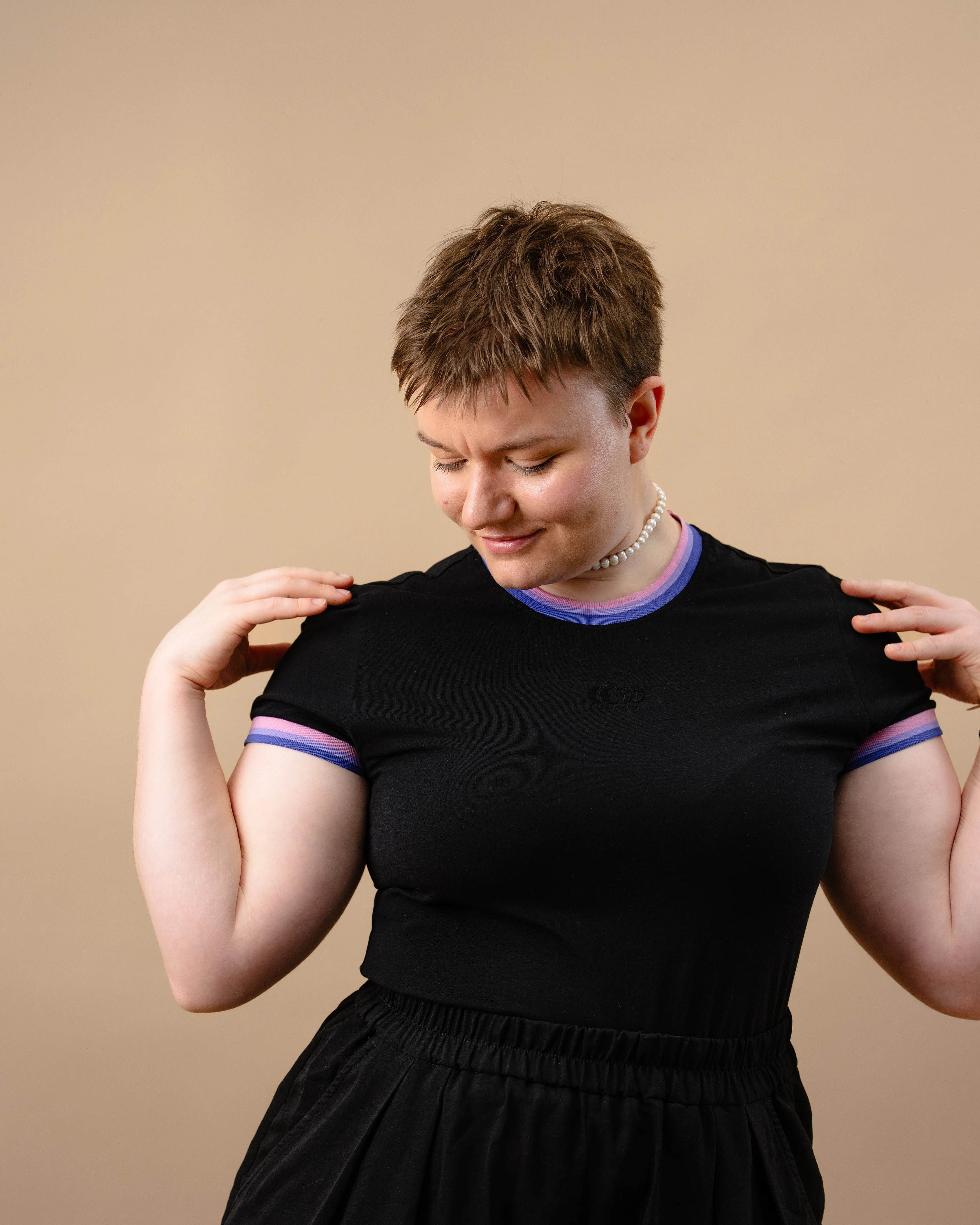 Model wearing a black Biweekly Babytee with bi pride flag trim on the collar and sleeves and black logo in the front, front view against a beige background