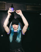 Model wearing a black Biweekly Babytee with bi pride flag trim on the collar and sleeves and black logo in the front, front view in a club scene, dancing