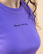 Detailshot of model wearing a lilac Biweekly tank top with black ‘Assume nothing’ text, side view against a beige background