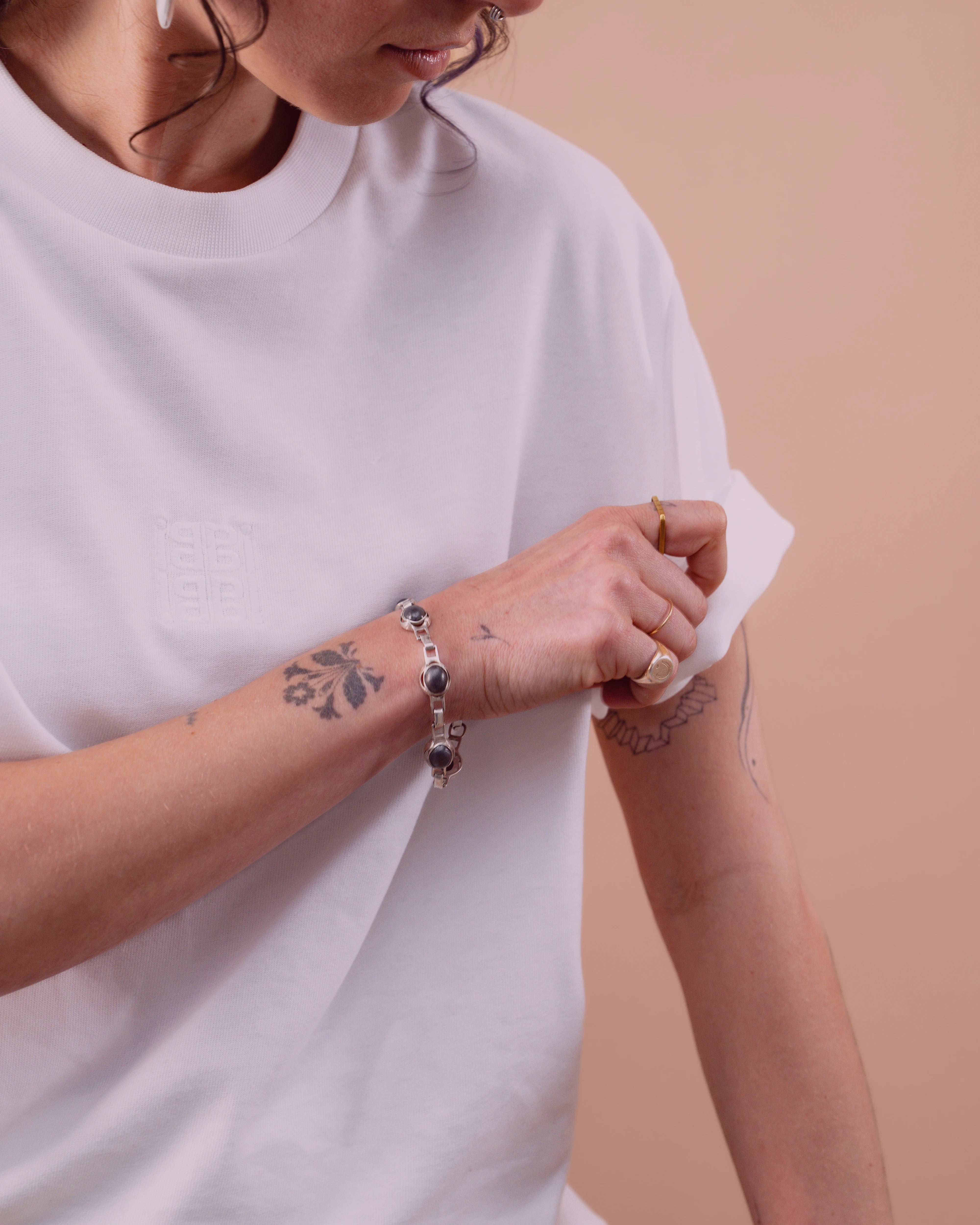 Detailshot of model adjusting her sleeve of a white Biweekly oversized Tee with subtle burgundy colour overlay 