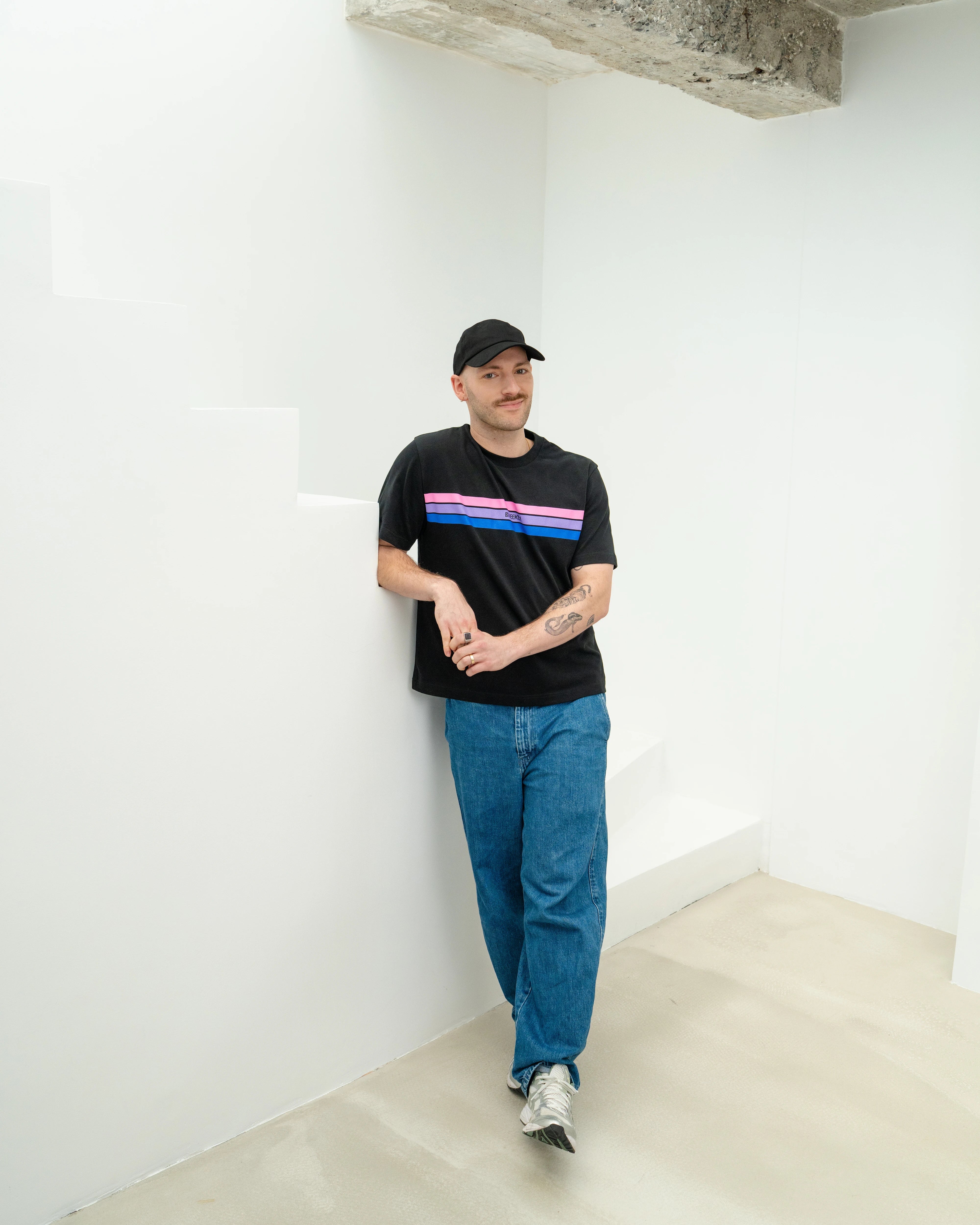 Model leaning against stairs wearing a black Biweekly cap full body shot front view against white background