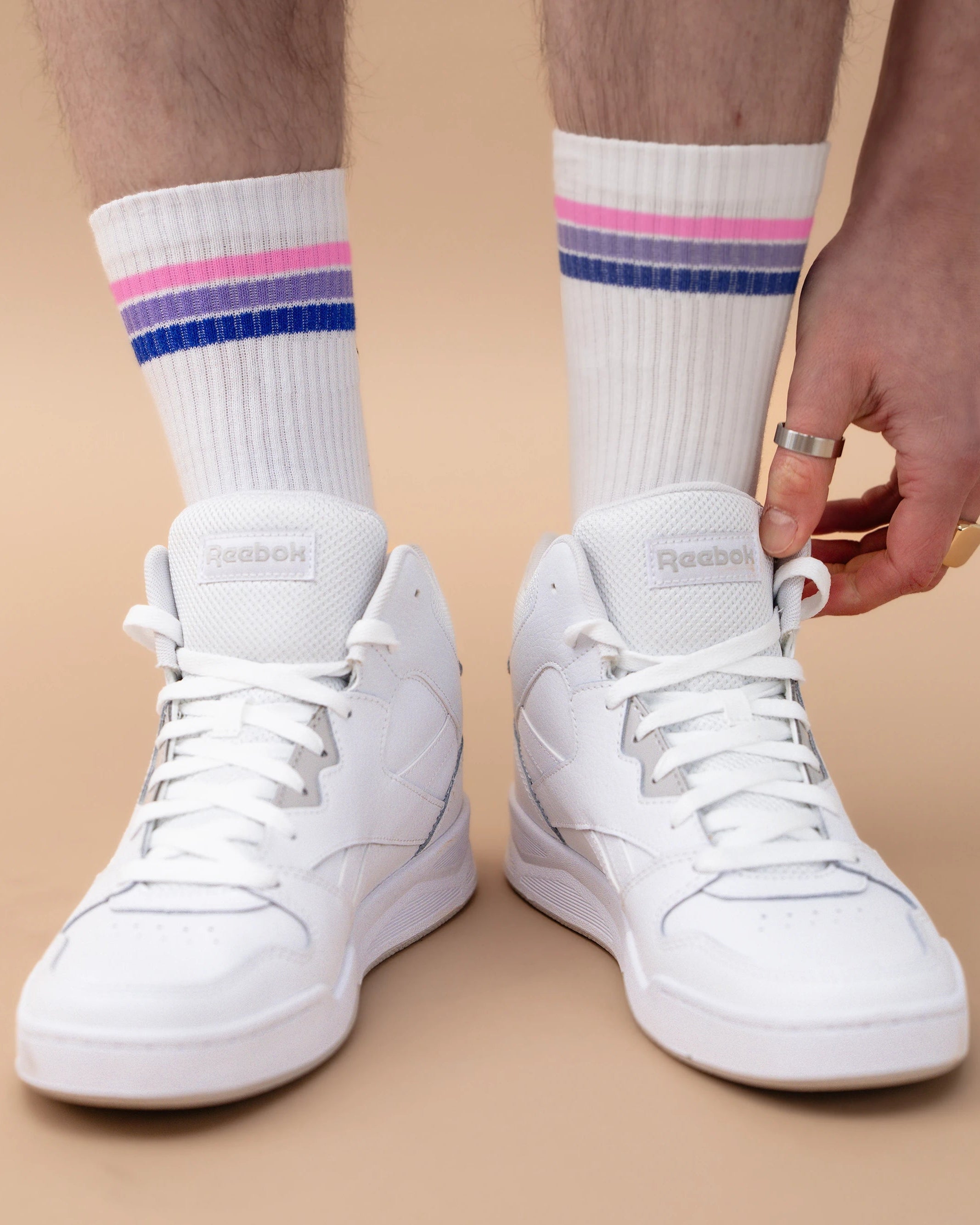 Model wearing white Biweekly socks with bi pride flag stripes, paired with white sneakers, against a beige background