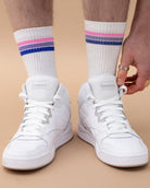Model wearing white Biweekly socks with bi pride flag stripes, paired with white sneakers, against a beige background