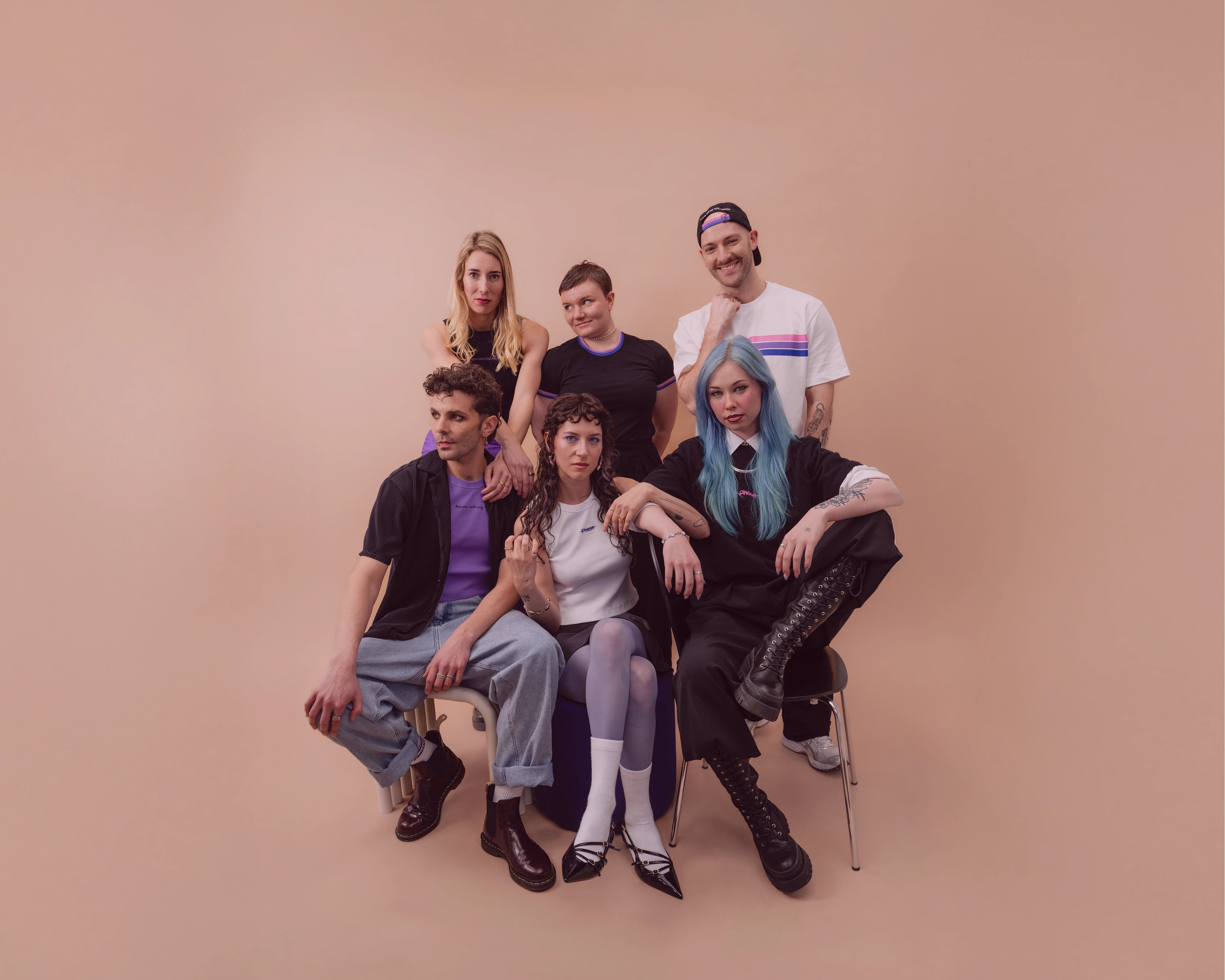 Group of diverse models wearing Biweekly clothing with graphic prints and bi pride color accents, posing together against a beige background with subtle transparent burgundy color overlay 