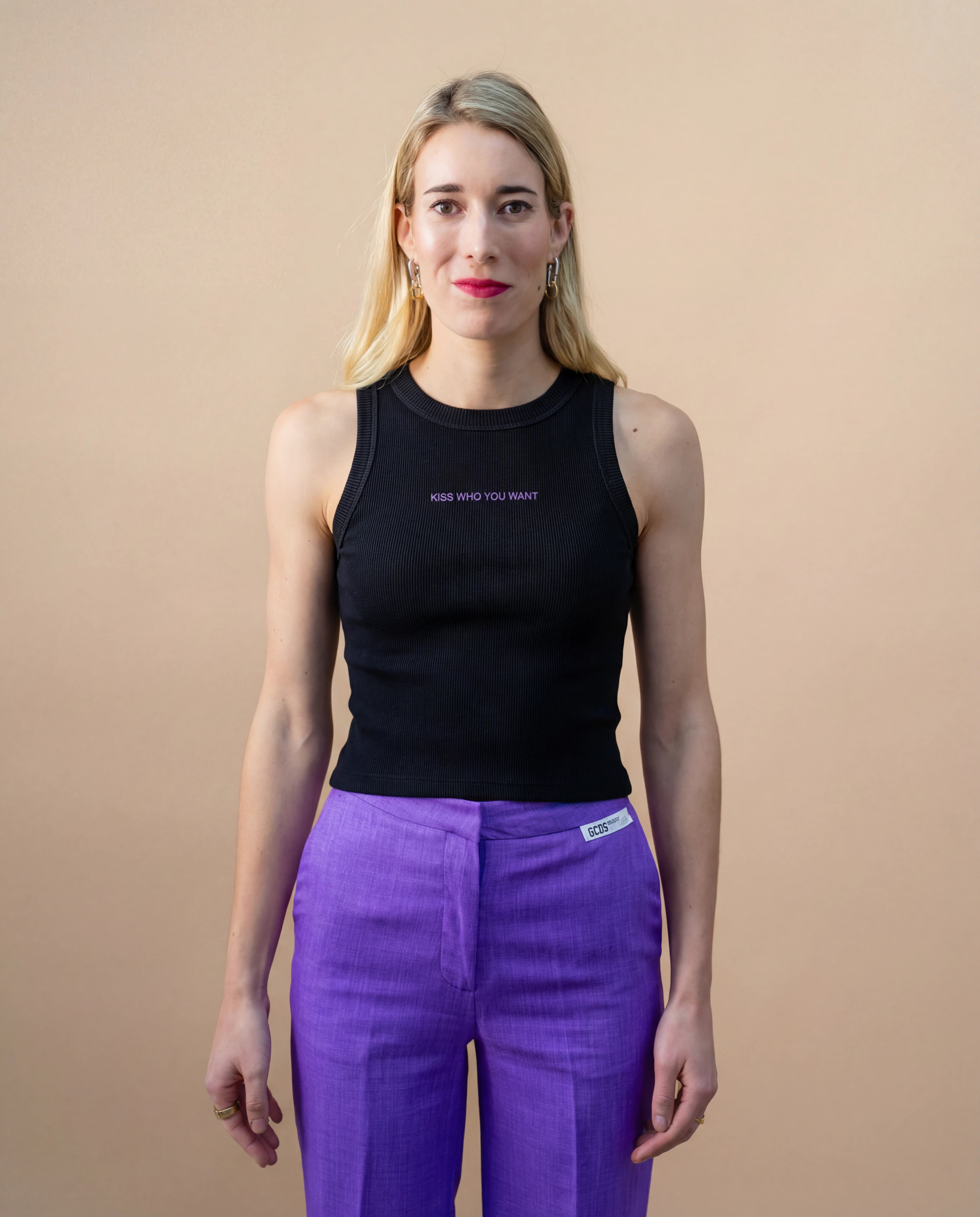 Model wearing a black Biweekly tank top with lilac ‘Kiss Who You Want’ text, front view against a beige background
