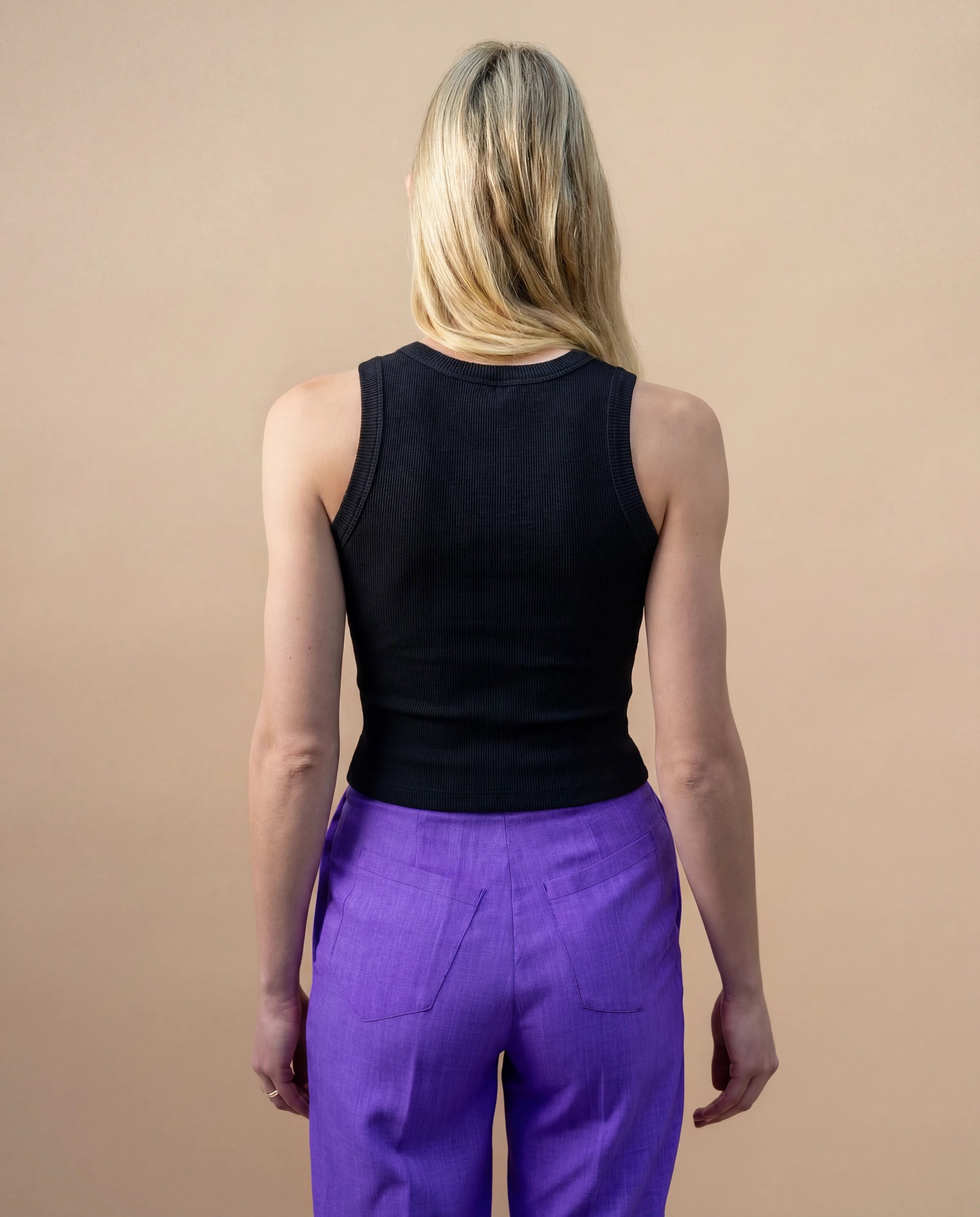 Model wearing a black Biweekly tank top, back view against a beige background