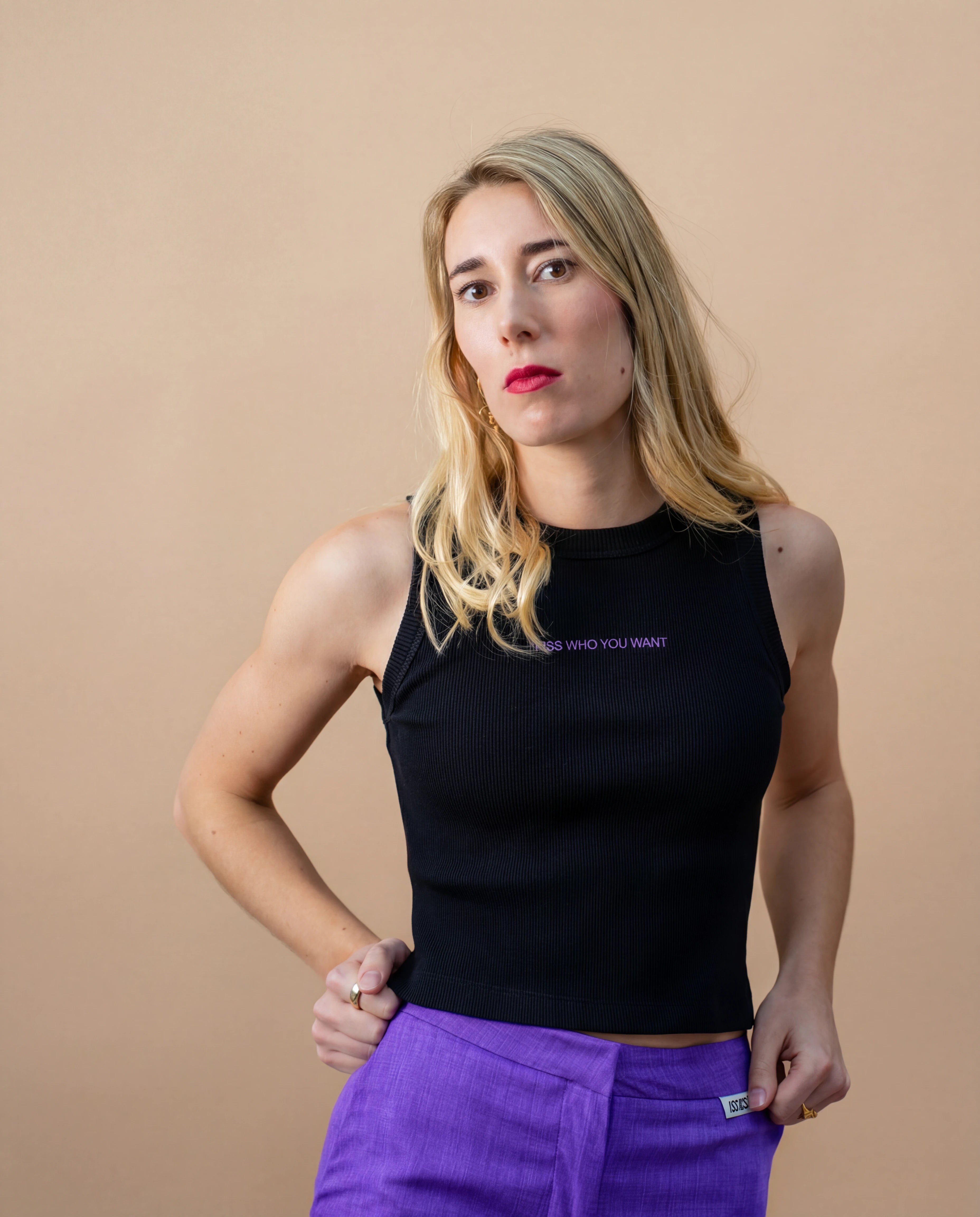 Model wearing a black Biweekly tank top with lilac ‘Kiss Who You Want’ text, front view against a beige background