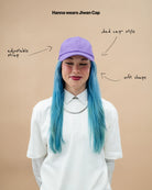 Model wearing a lilac Biweekly cap, front view against a beige background with text: "adjustable straps, dad cap style, soft shape" arranged with arrows