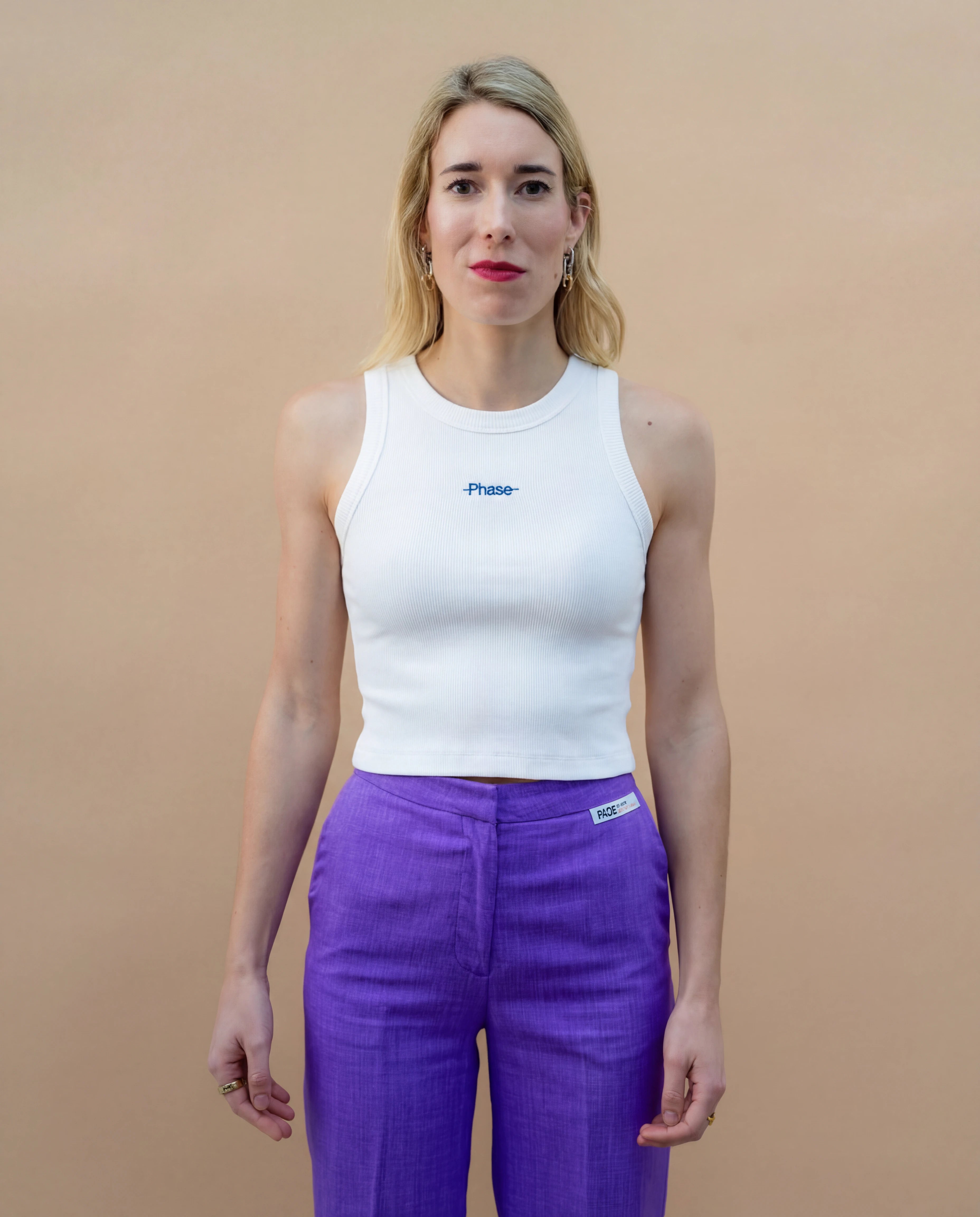 Model wearing a white Biweekly tank top with blue ‘Phase’ text that is crossed out, front view against a beige background