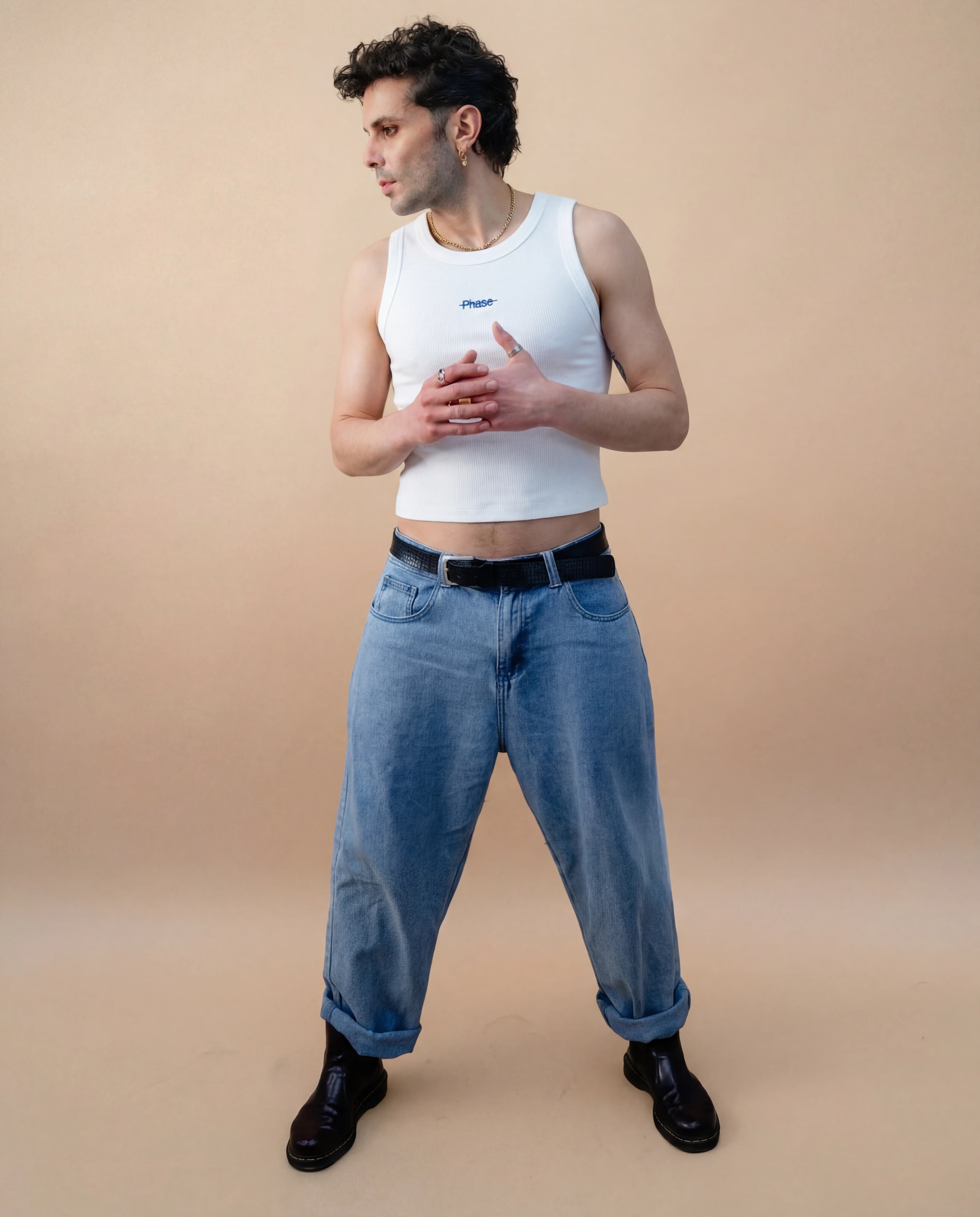 Model wearing a white Biweekly tank top with blue ‘Phase’ text that is crossed out, full body shot front view against a beige background